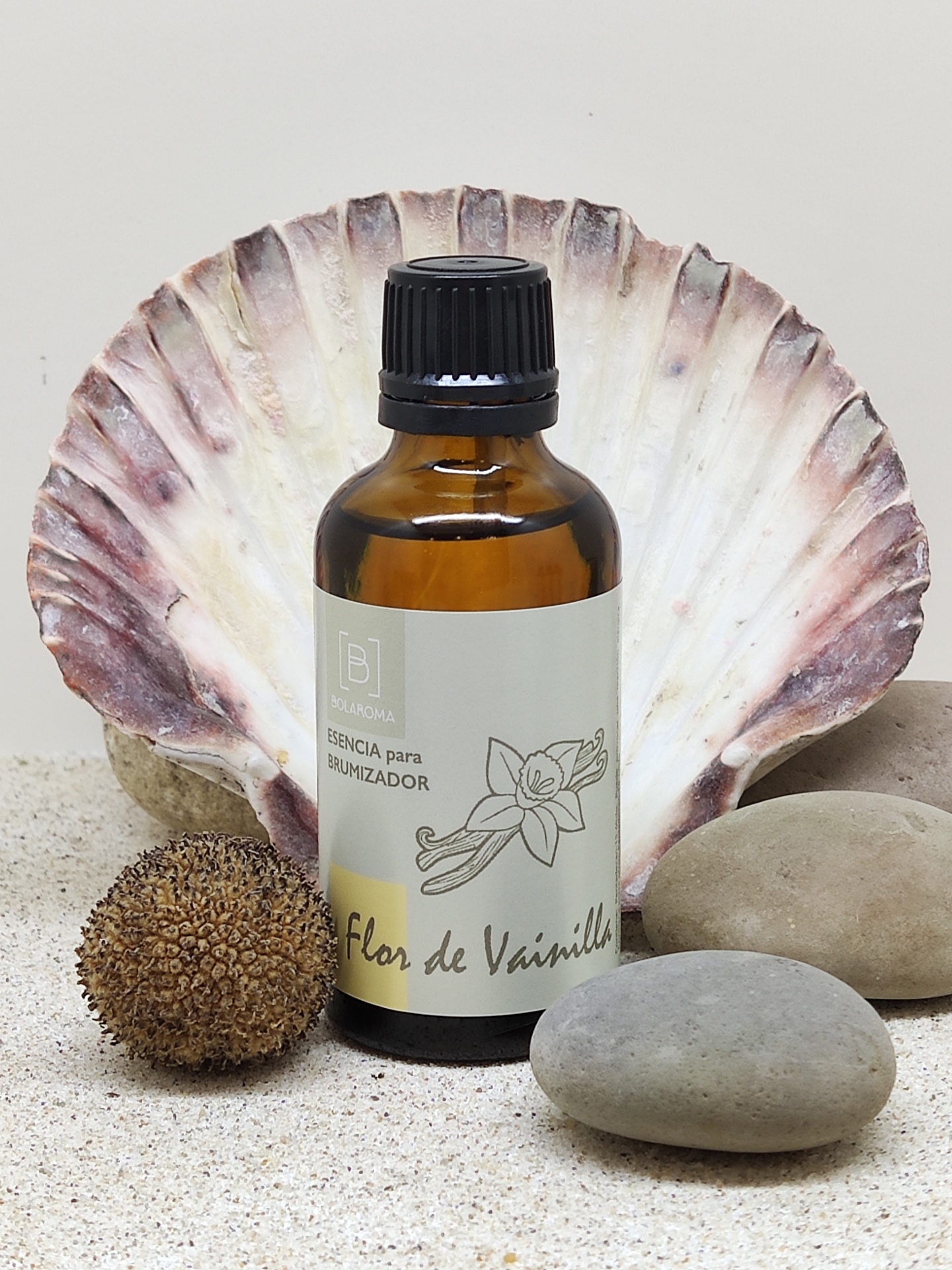 Frasco âmbar de essência para umidificador com tampa preta e etiqueta branca, rodeado por pedras, concha e areia