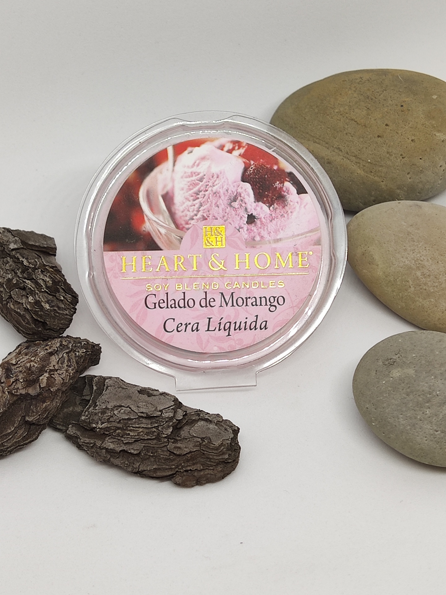 Pote de cera líquida para velas com rótulo de gelado de morango sobre fundo branco com pedras.