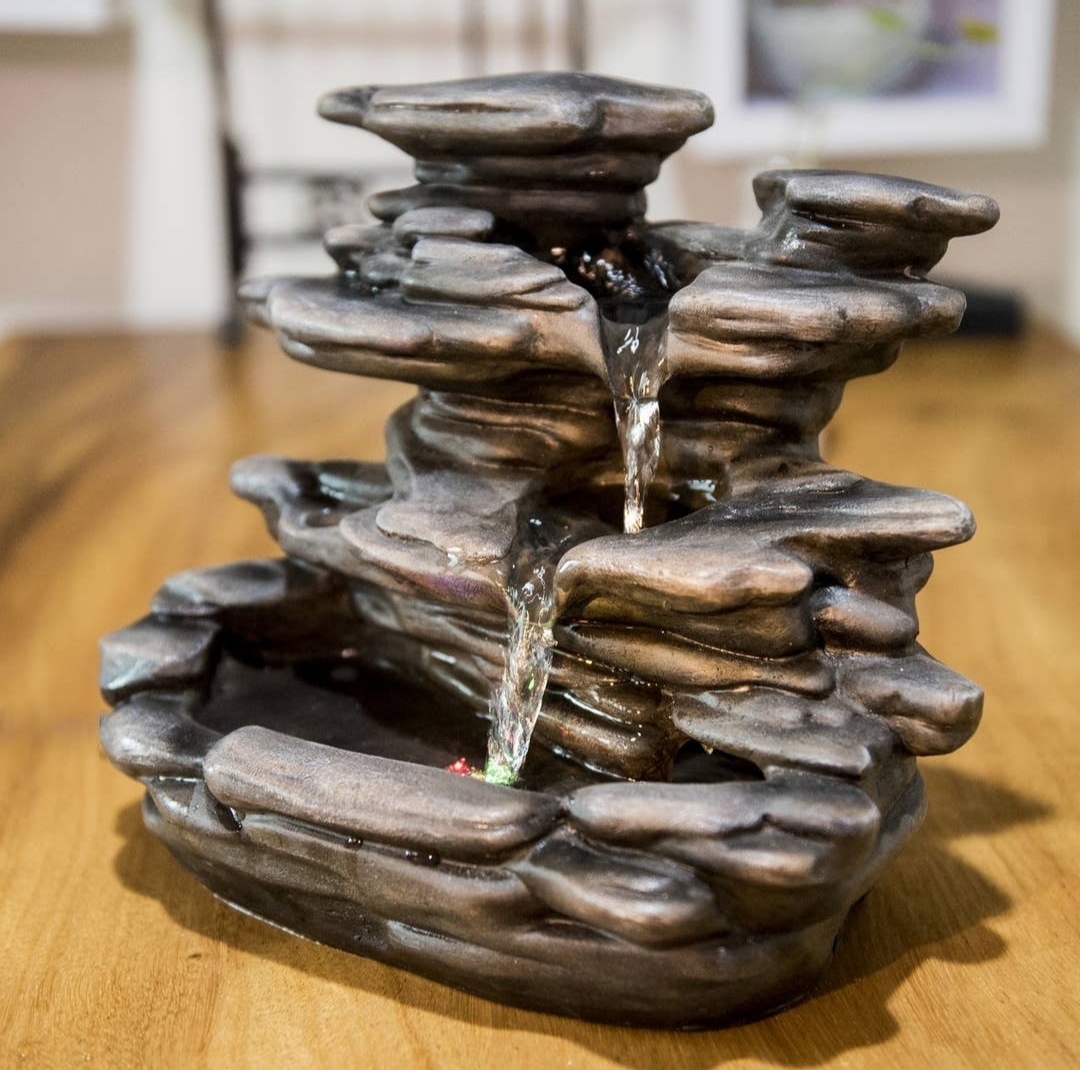 Fonte decorativa cinza-escuro com água a cair em cascata sobre madeira