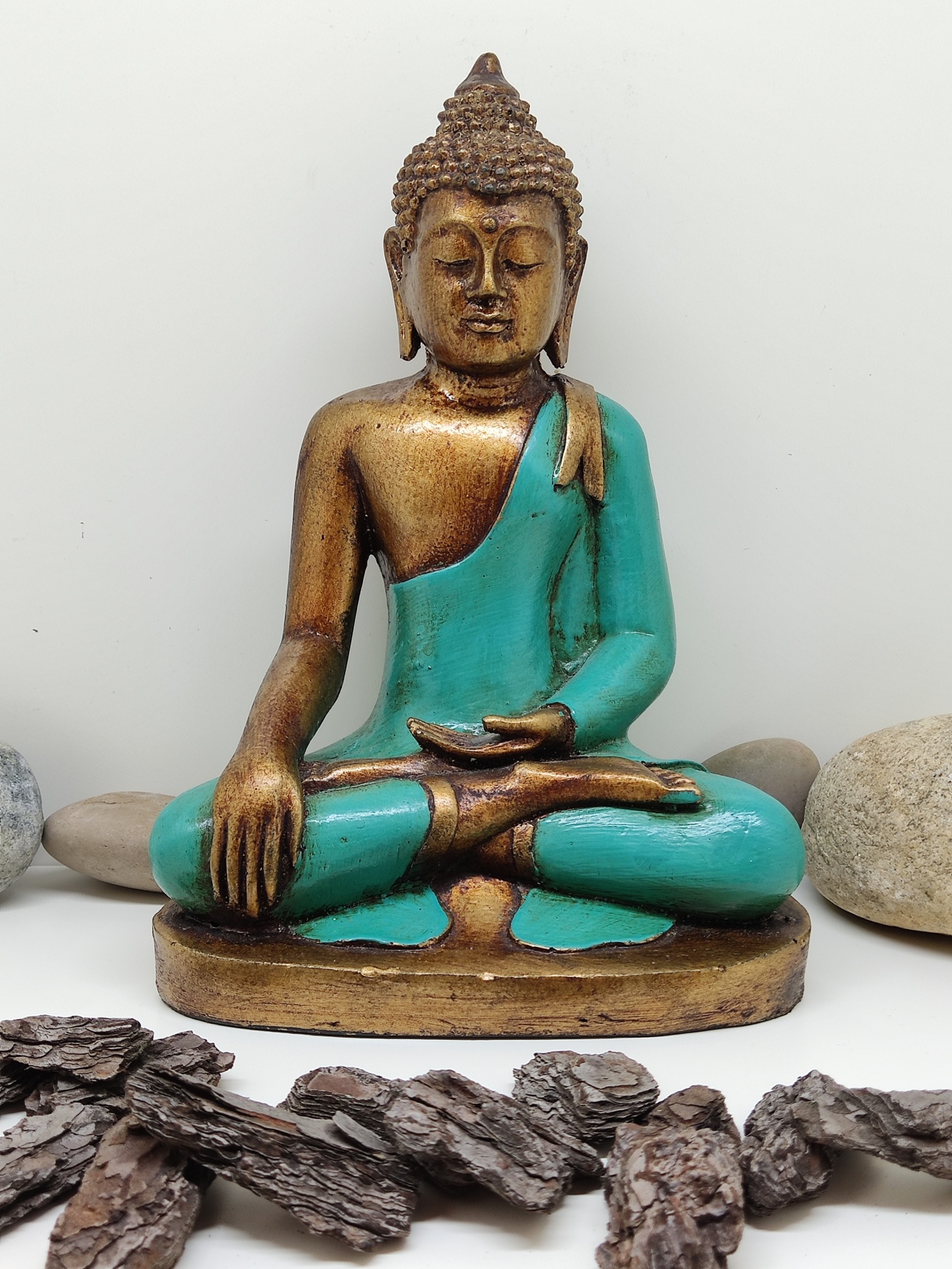 Estátua de Buda dourada e turquesa rodeada de pedras e casca de árvore