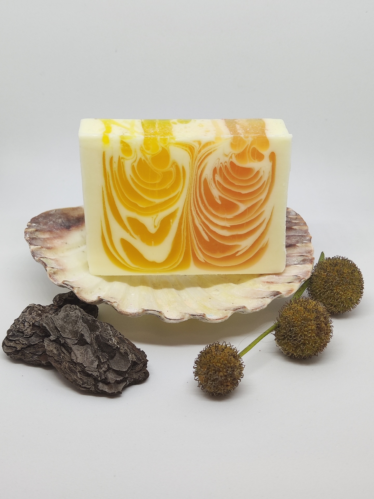 Sabonete artesanal com padrões amarelo e laranja numa concha com casca de árvore e bolbos secos