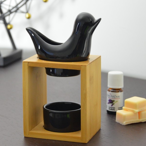 Difusor de aromaterapia pássaro preto sobre suporte de madeira com óleo essencial e cera