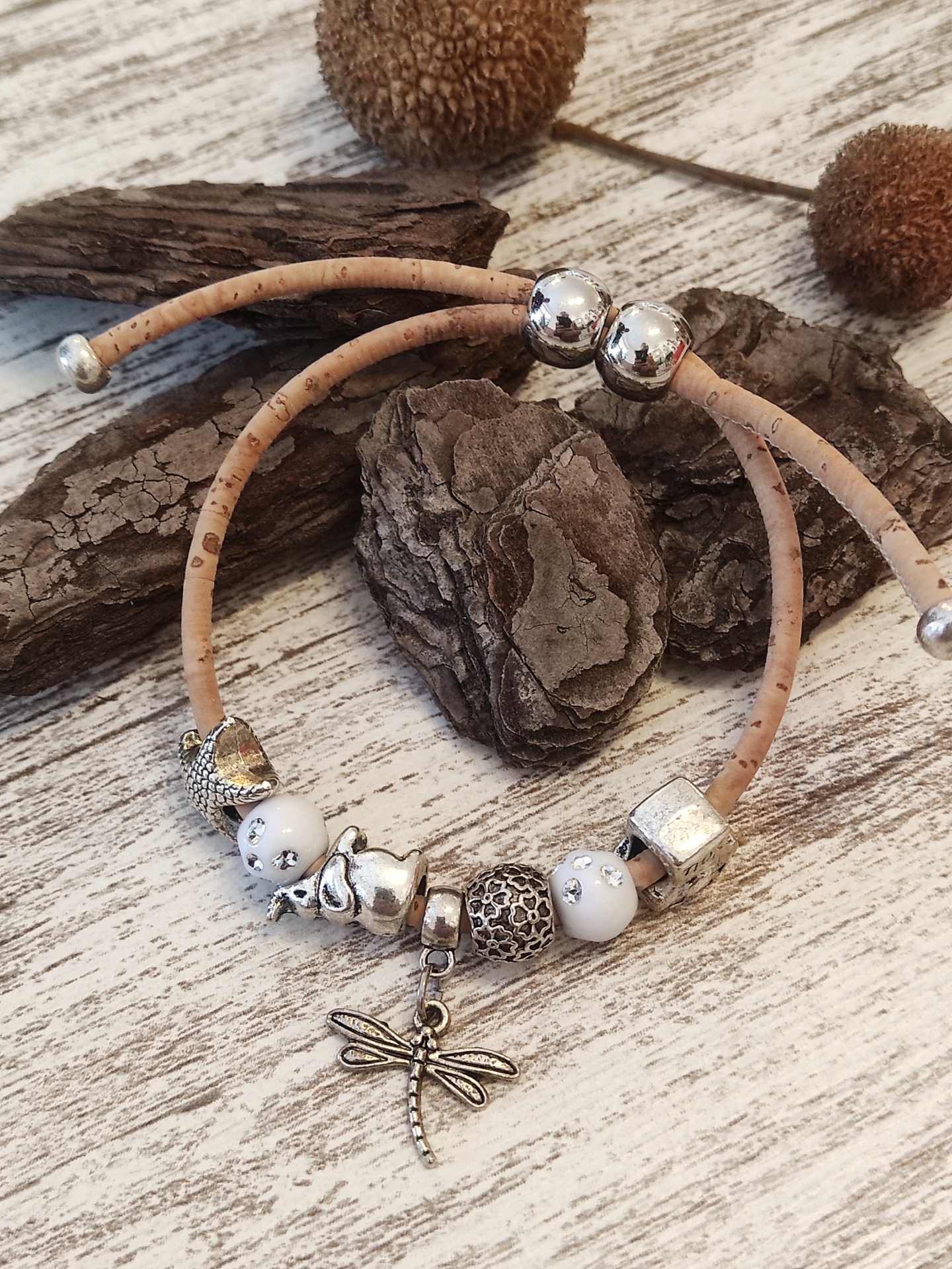 Pulseira de cortiça bege com contas decorativas e pingente de libélula sobre madeira clara