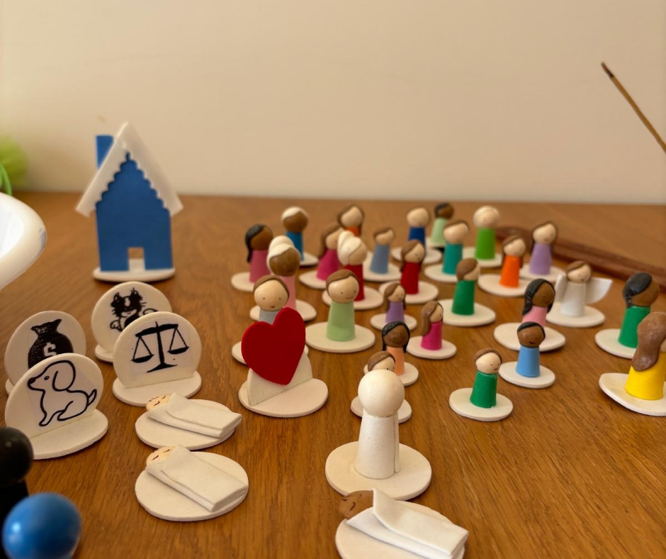 Peças de jogo de madeira coloridas em forma de pessoas e símbolos, dispostas sobre mesa de madeira