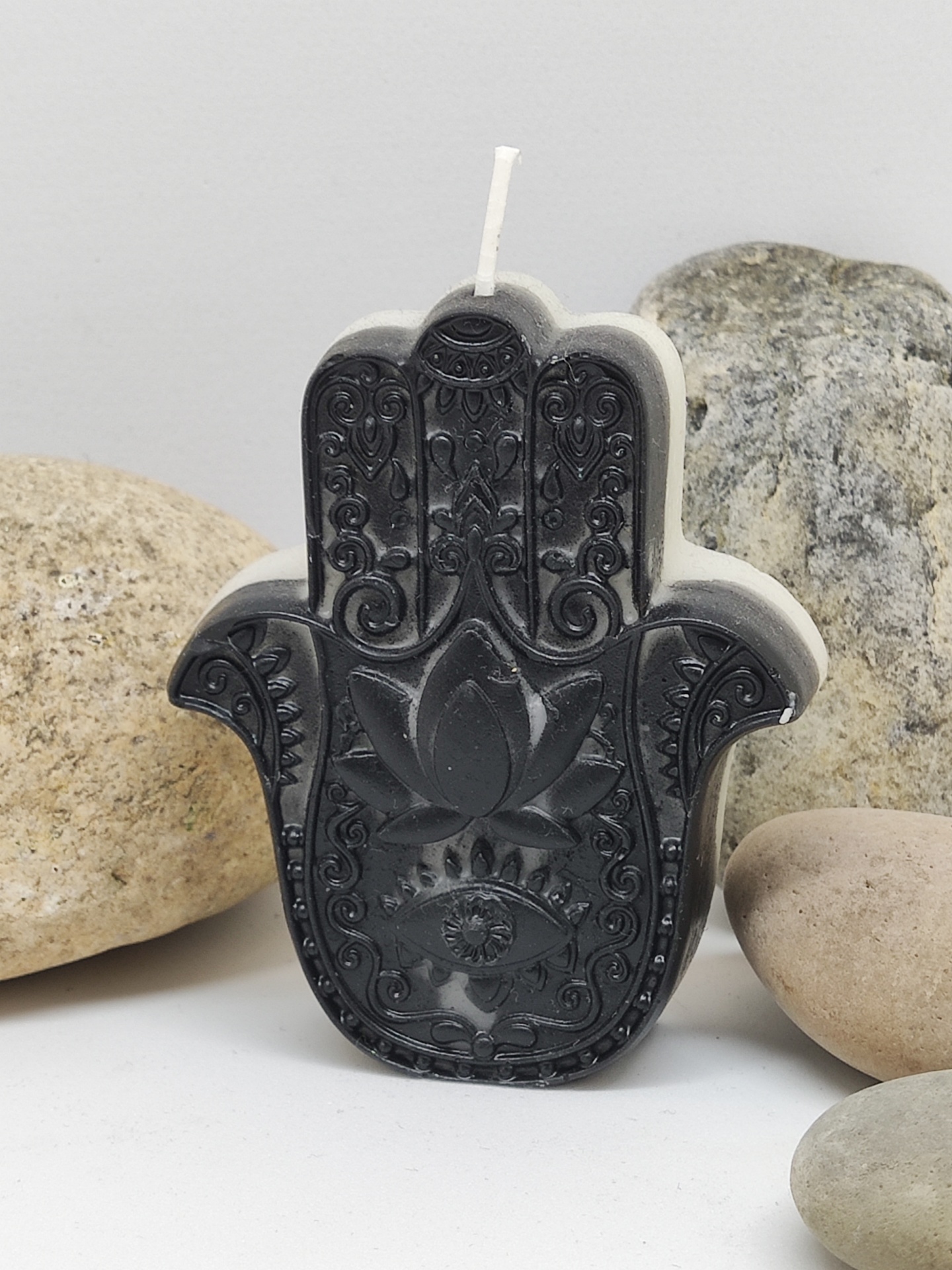 Vela em forma de mão de Hamsá com padrões detalhados e pedras ao redor