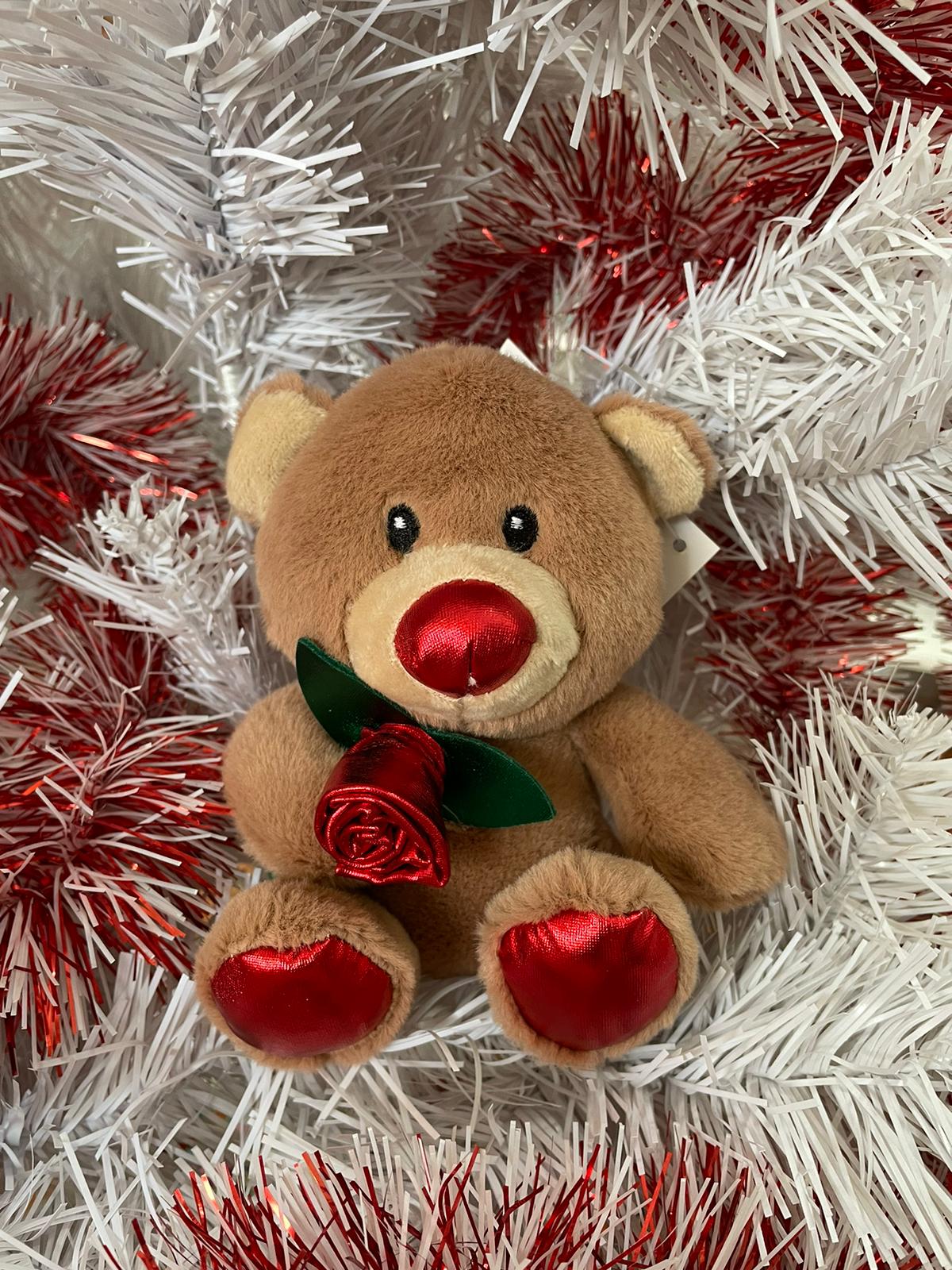 Ursinho de pelúcia castanho claro com nariz e patas vermelhos em fundo de ramos brancos e vermelhos