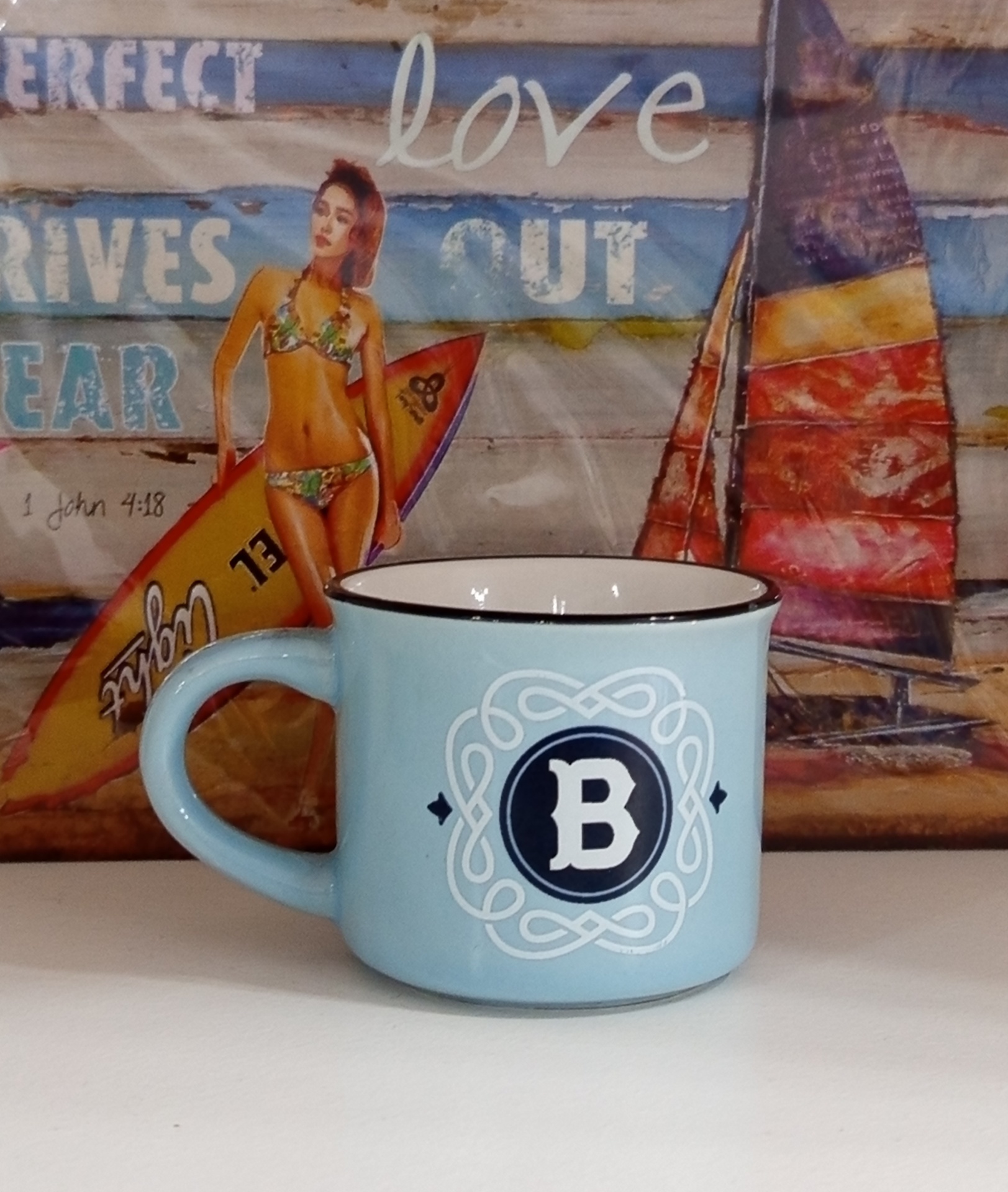 Caneca azul com letra B em primeiro plano e cartaz colorido ao fundo