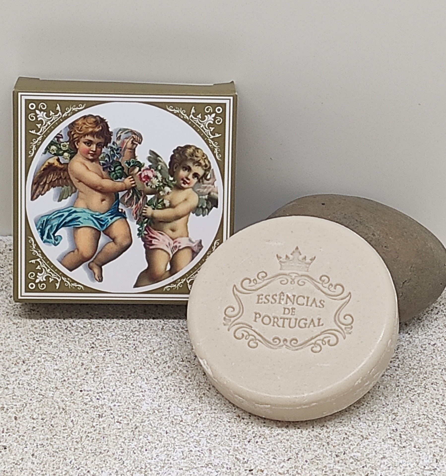 Sabonete redondo bege com embalagem decorada com anjos e texto essências de Portugal.