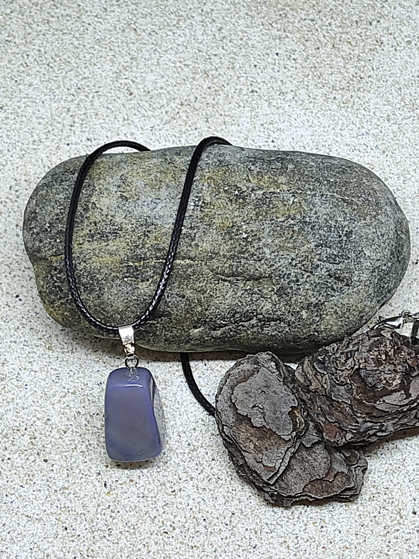 Colar com pendente de pedra azul translúcida e cordão preto sobre pedra e cascas