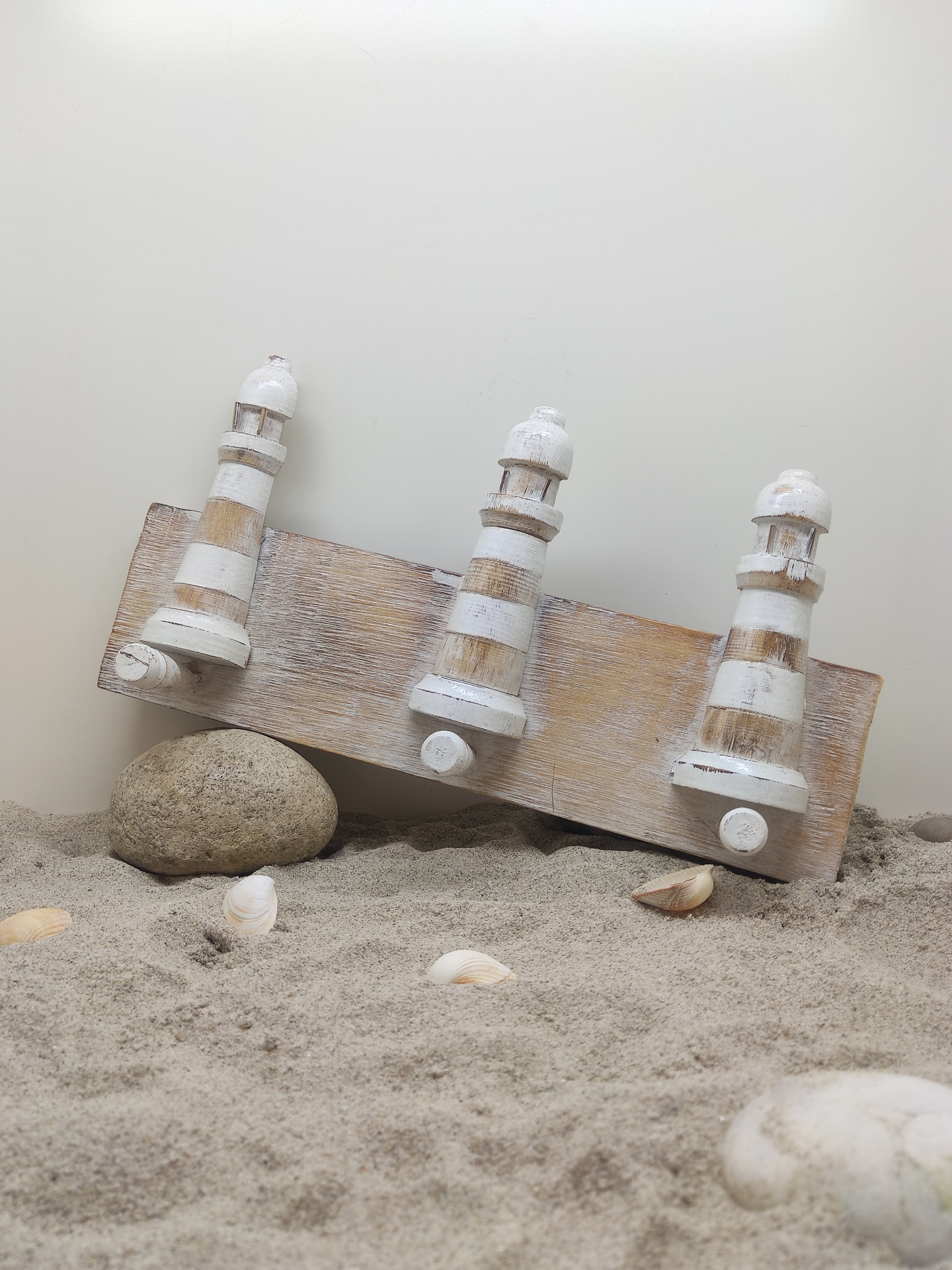 Três ganchos decorativos de madeira branca com efeito envelhecido sobre base de madeira na areia