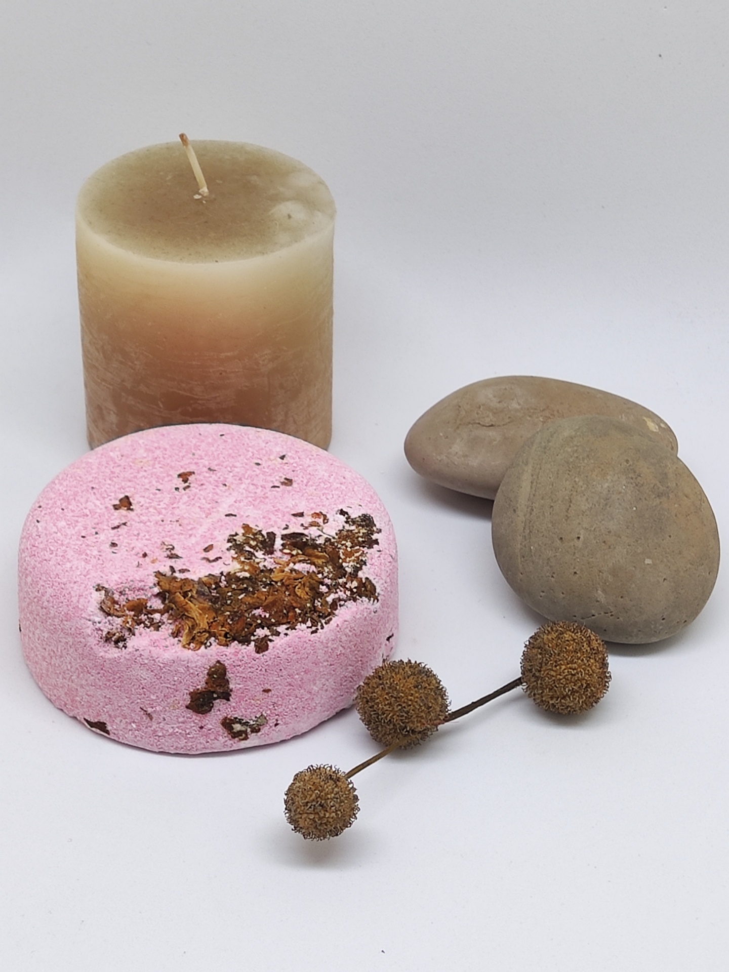 vela castanha, pastilha rosa com ervas, pedras castanhas e galho seco num fundo branco