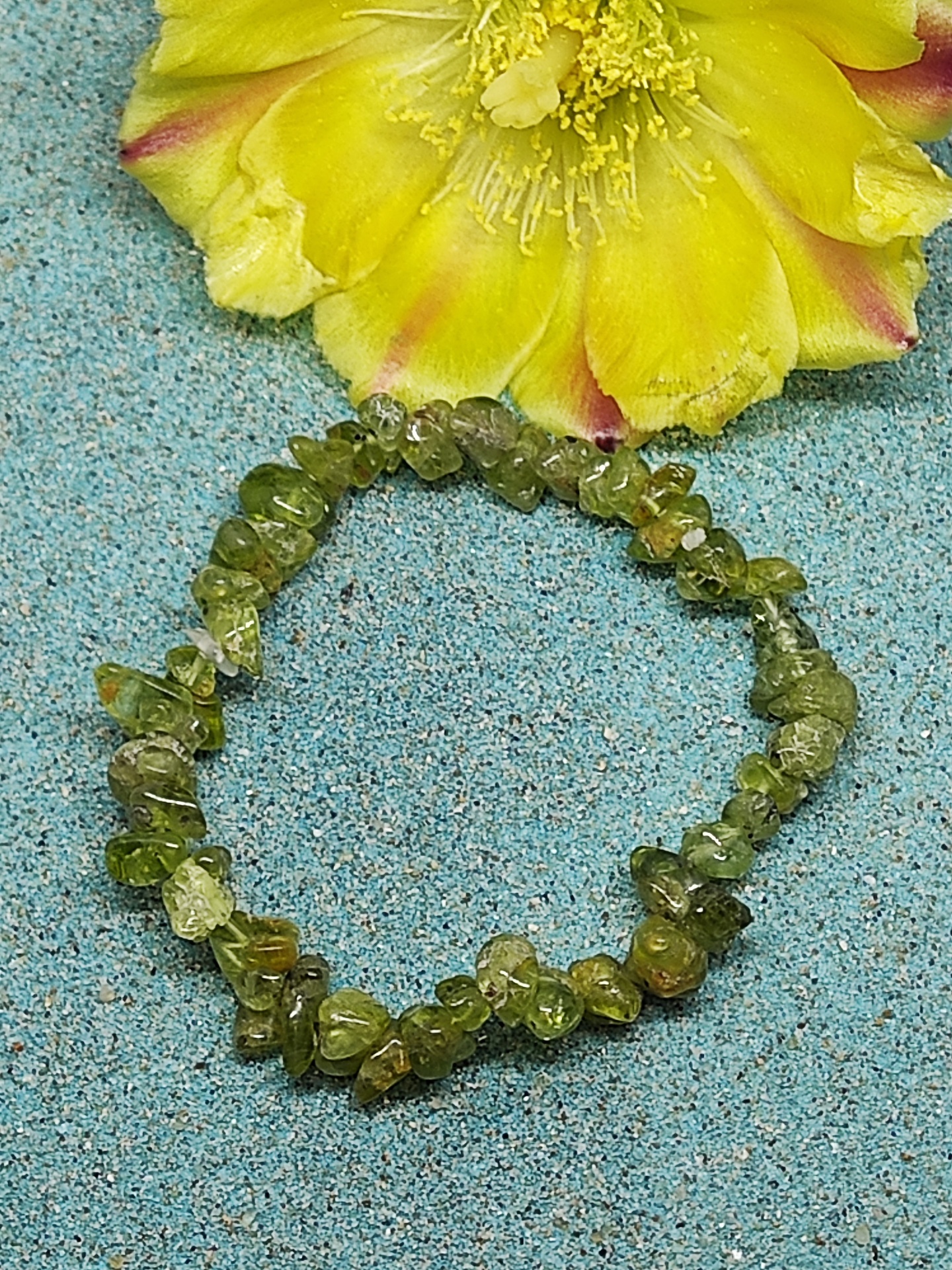 Bracelete de pedras verdes sobre superfície azul com flor amarela