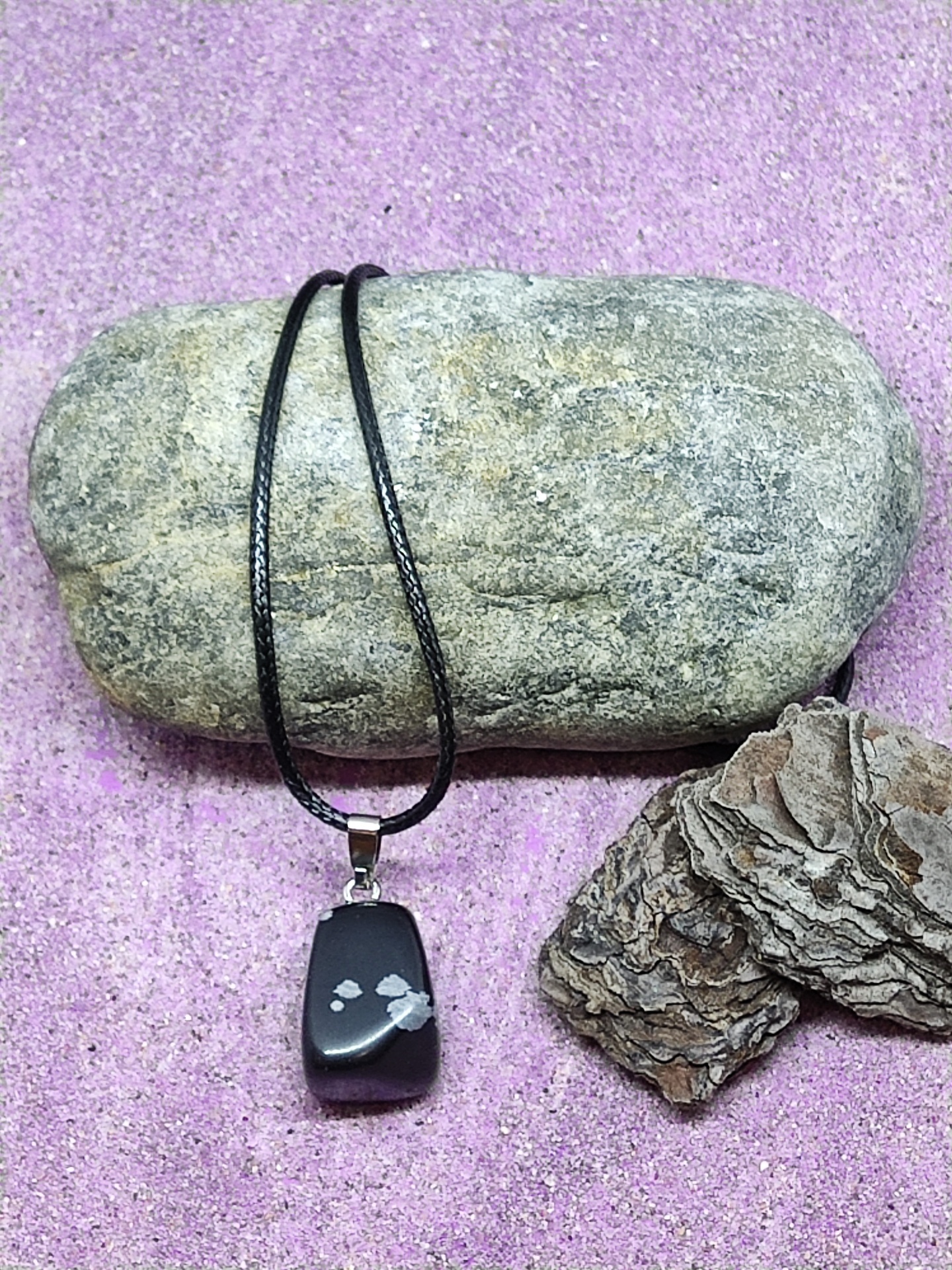 Colar com pendente preto e branco sobre pedra cinzenta e fundo rosa
