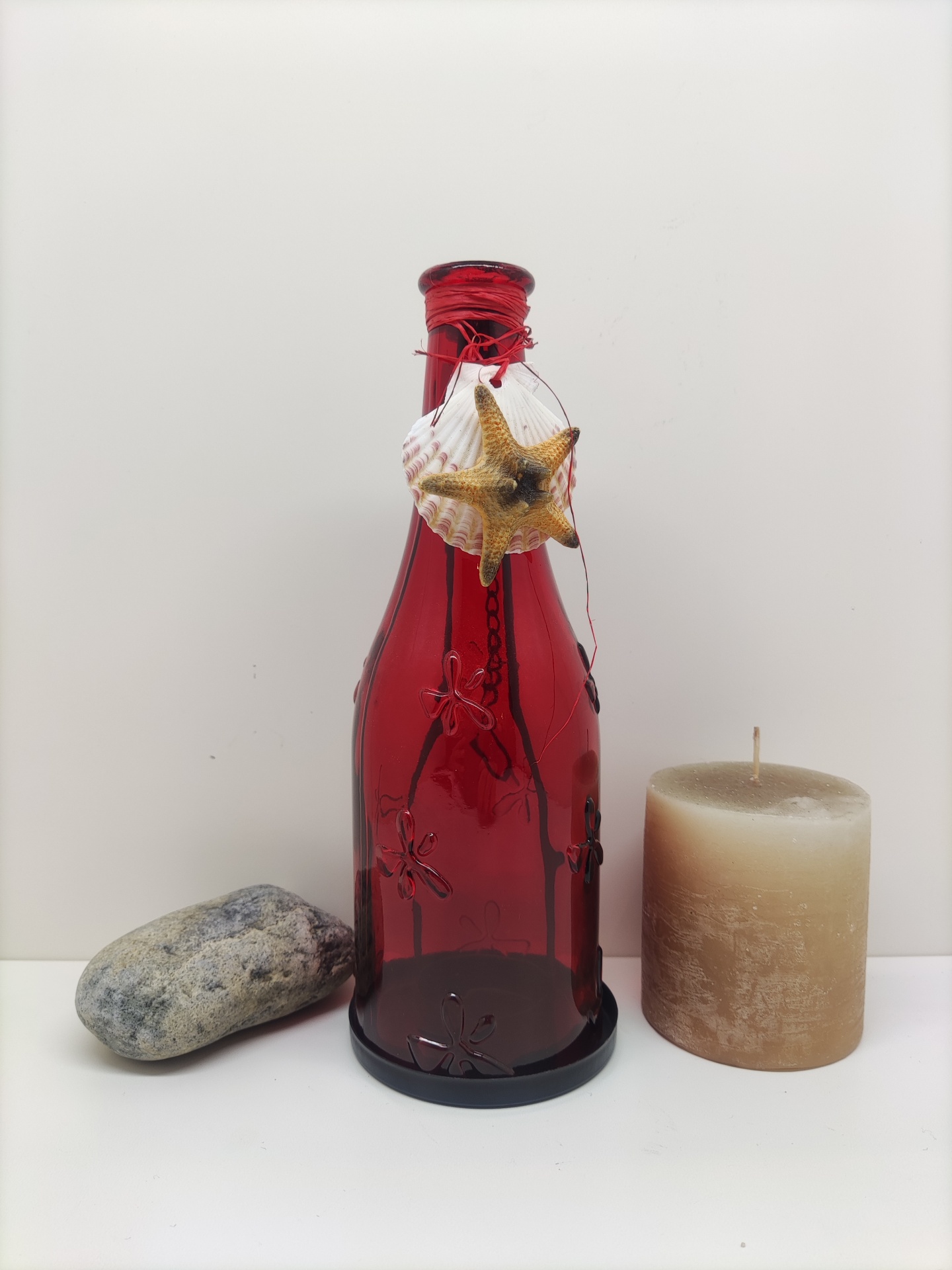Garrafa decorativa vermelha com enfeites marinhos, vela castanha e pedra cinzenta