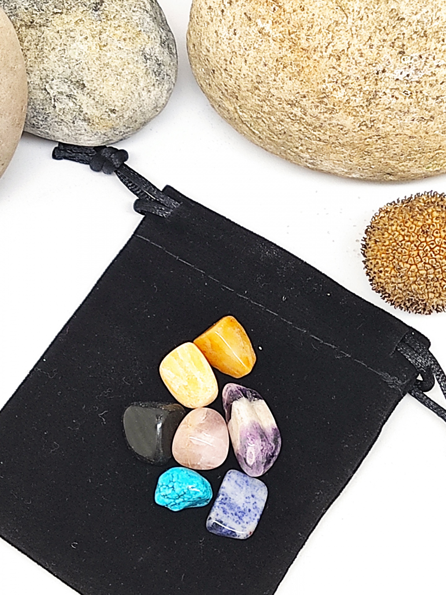 Sete pedras polidas variadas sobre saco de tecido preto com pedras naturais ao redor