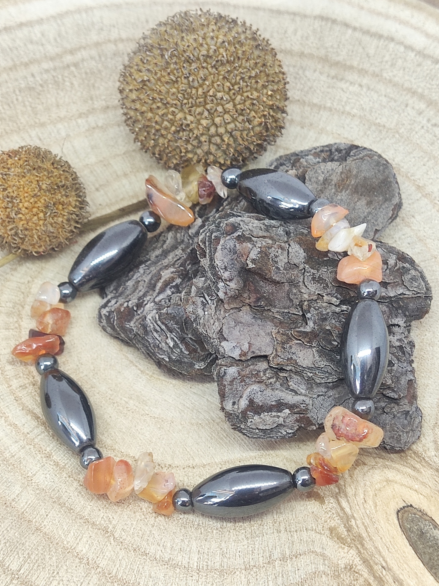 Pulseira com contas pretas e pedras laranja sobre casca de árvore