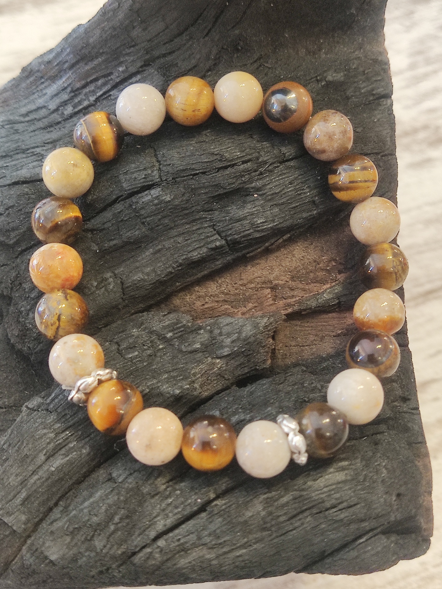 Pulseira de contas redondas em tons terrosos com detalhes metálicos sobre superfície de madeira preta.