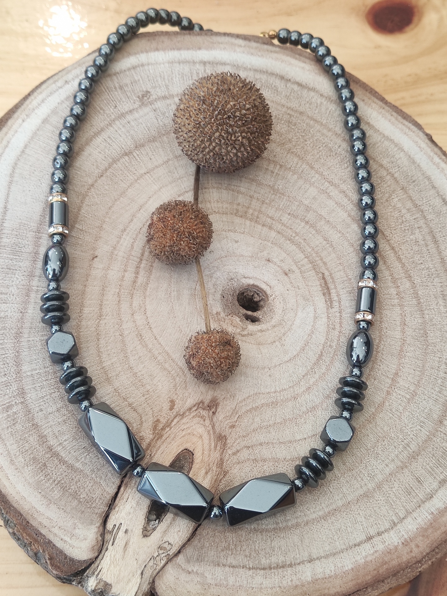 Colar preto brilhante de contas variadas sobre base de madeira circular com frutos secos marrons