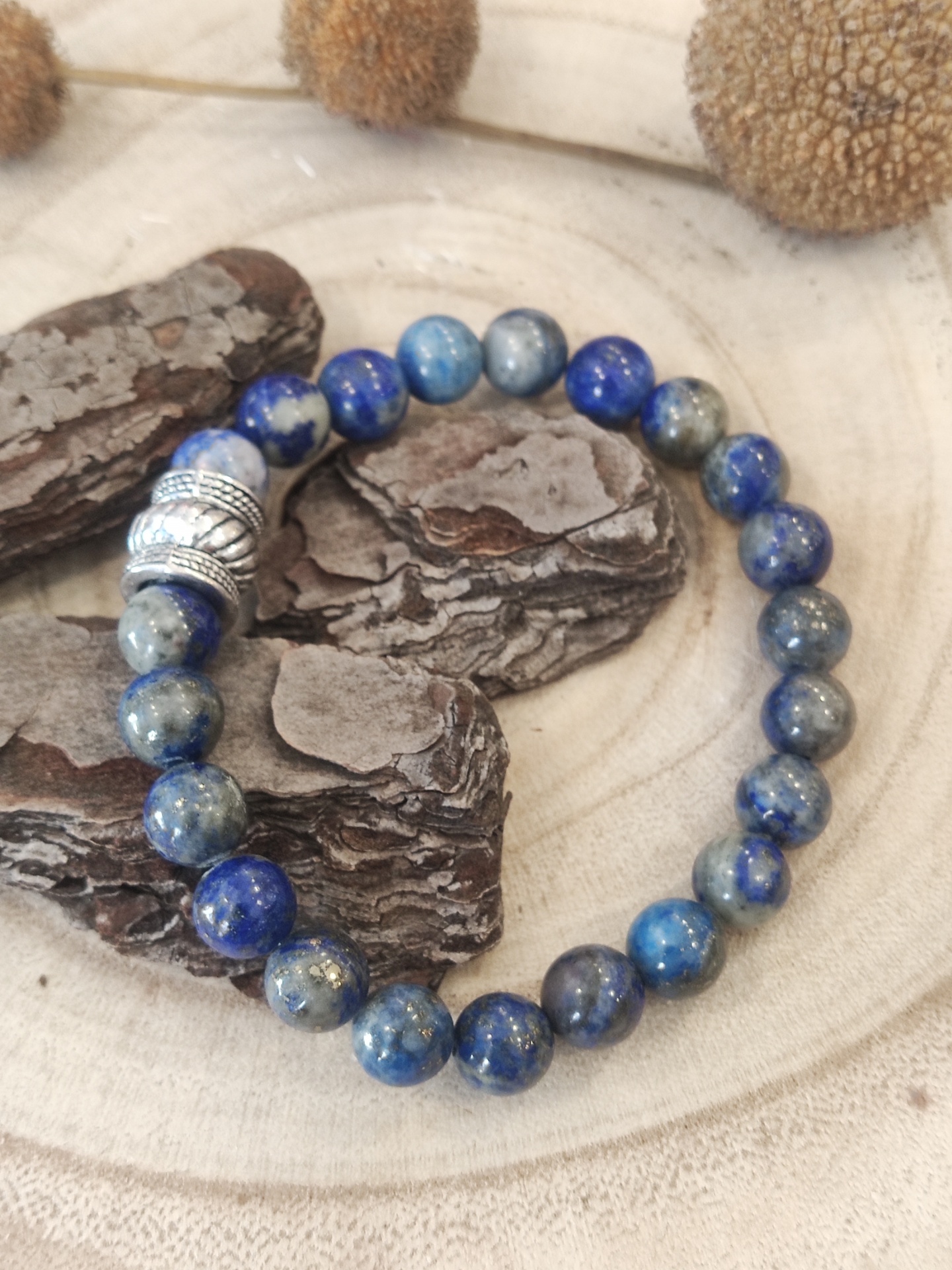 pulseira de contas azuis com separador metálico sobre fundo de madeira e casca