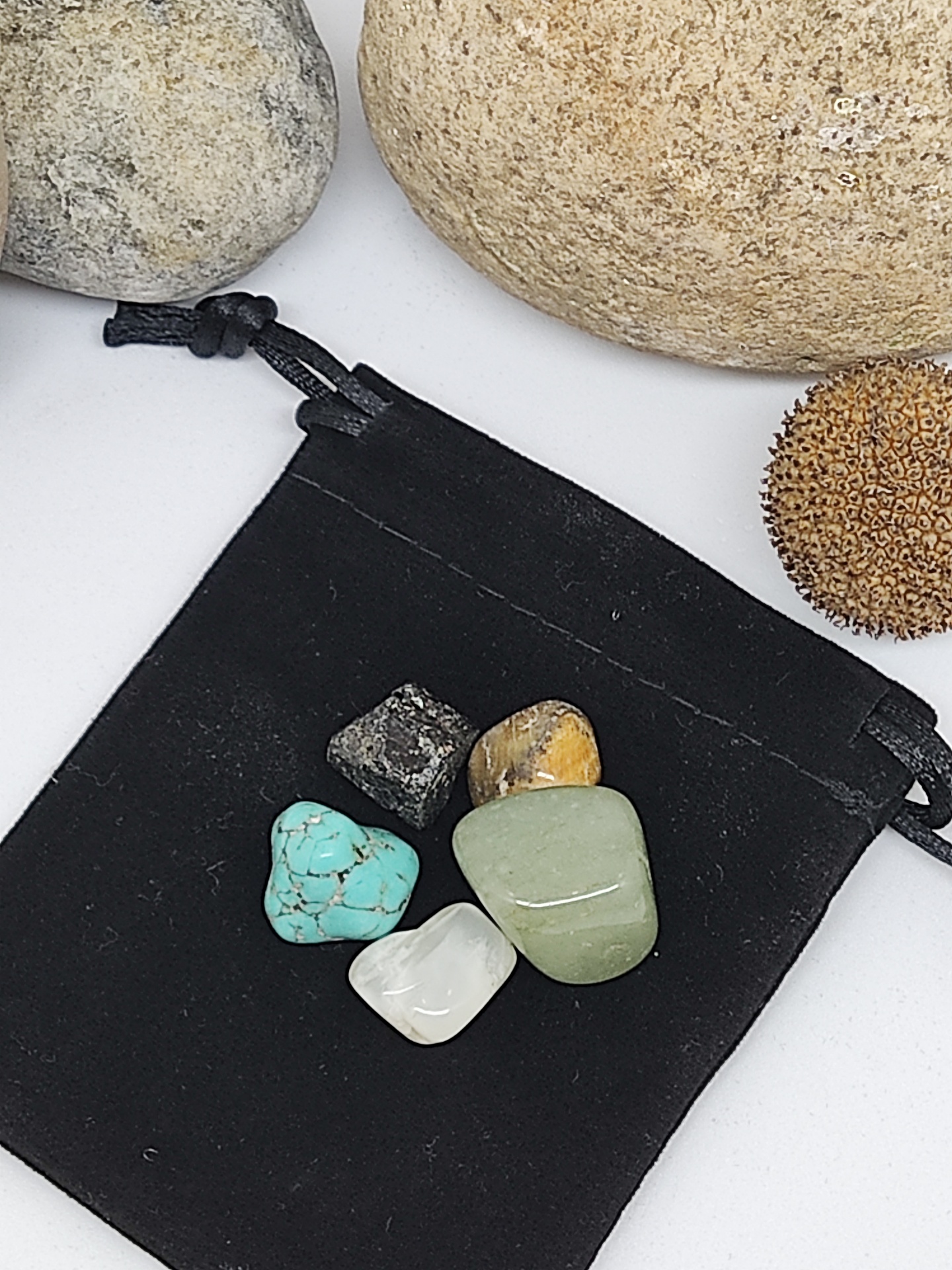 Cinco pedras coloridas polidas sobre saco preto de tecido com pedras maiores ao fundo