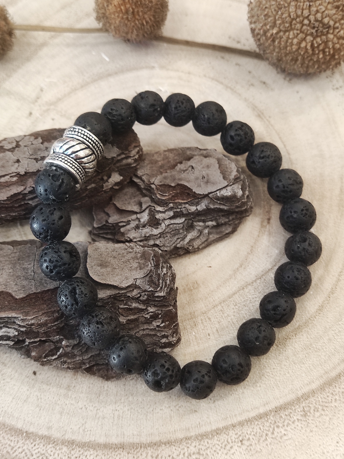 Pulseira de contas pretas porosas e conta prateada sobre superfície de madeira clara