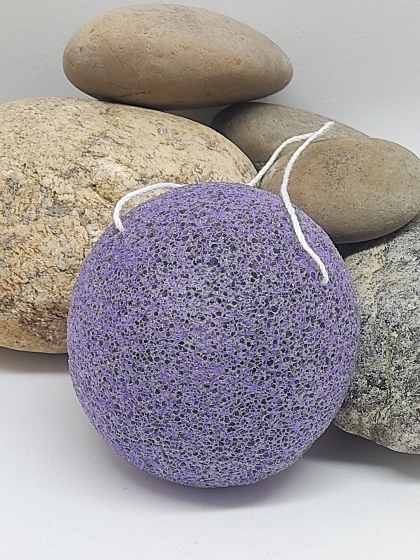 Esponja natural roxa com cordão branco sobre pedras lisas variadas