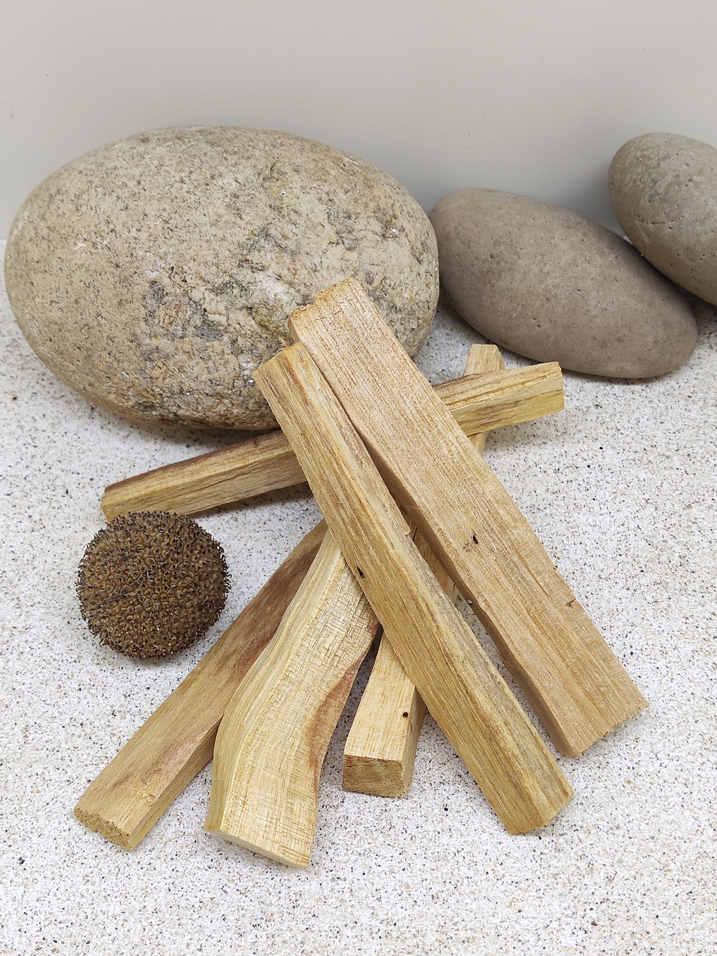 Pedaços de madeira claros empilhados sobre areia com pedras cinzentas e uma bola marrom