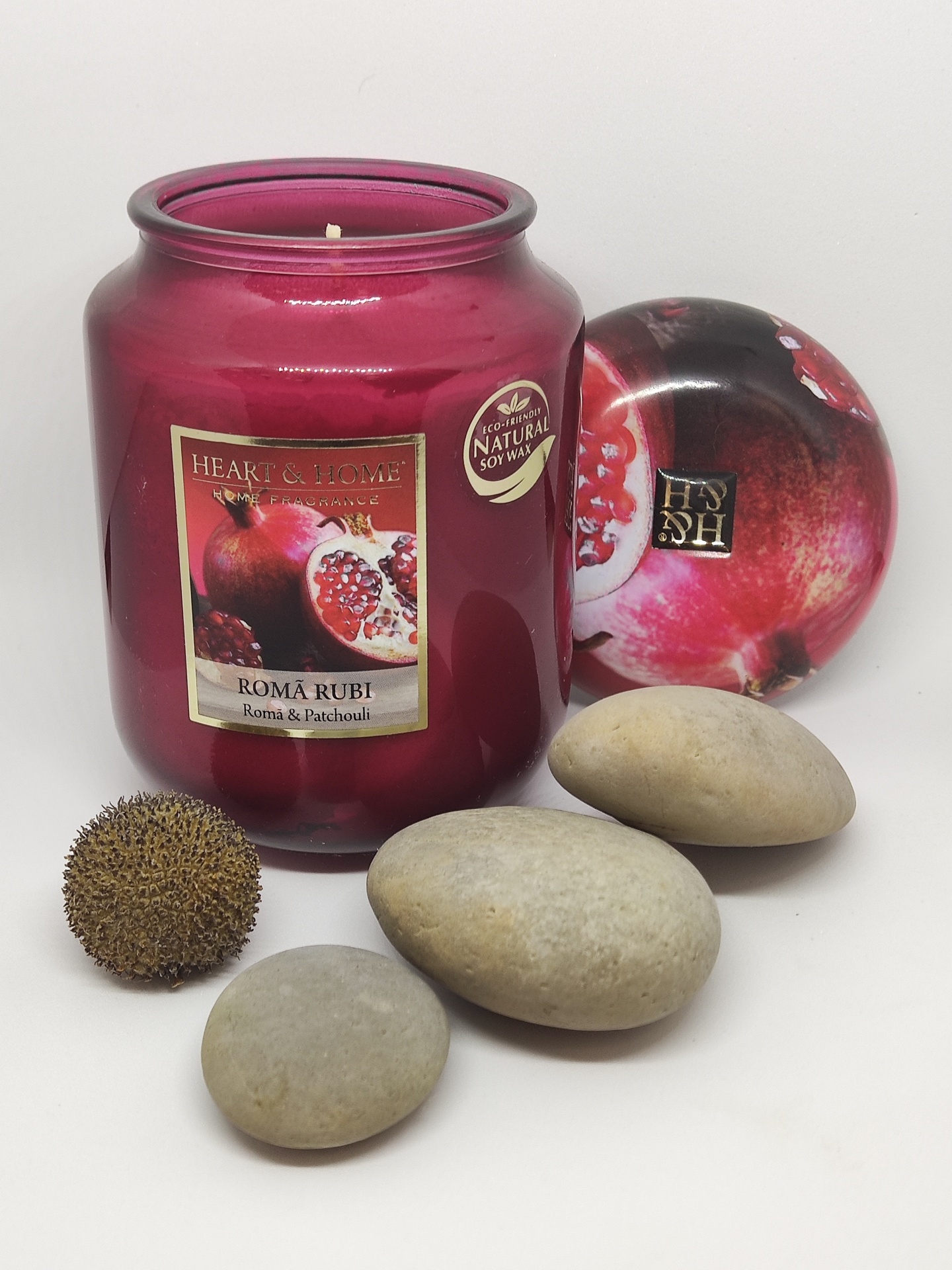 Vela perfumada em frasco vermelho com tampa de romã e pedras decorativas cinzentas e castanhas