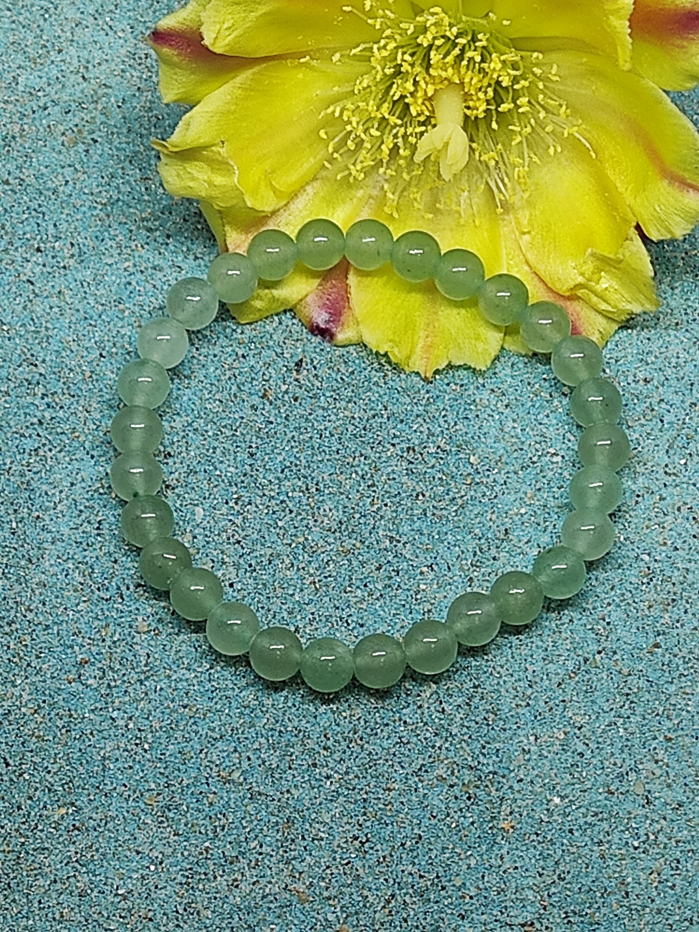 Pulseira de contas verdes com flor amarela ao fundo