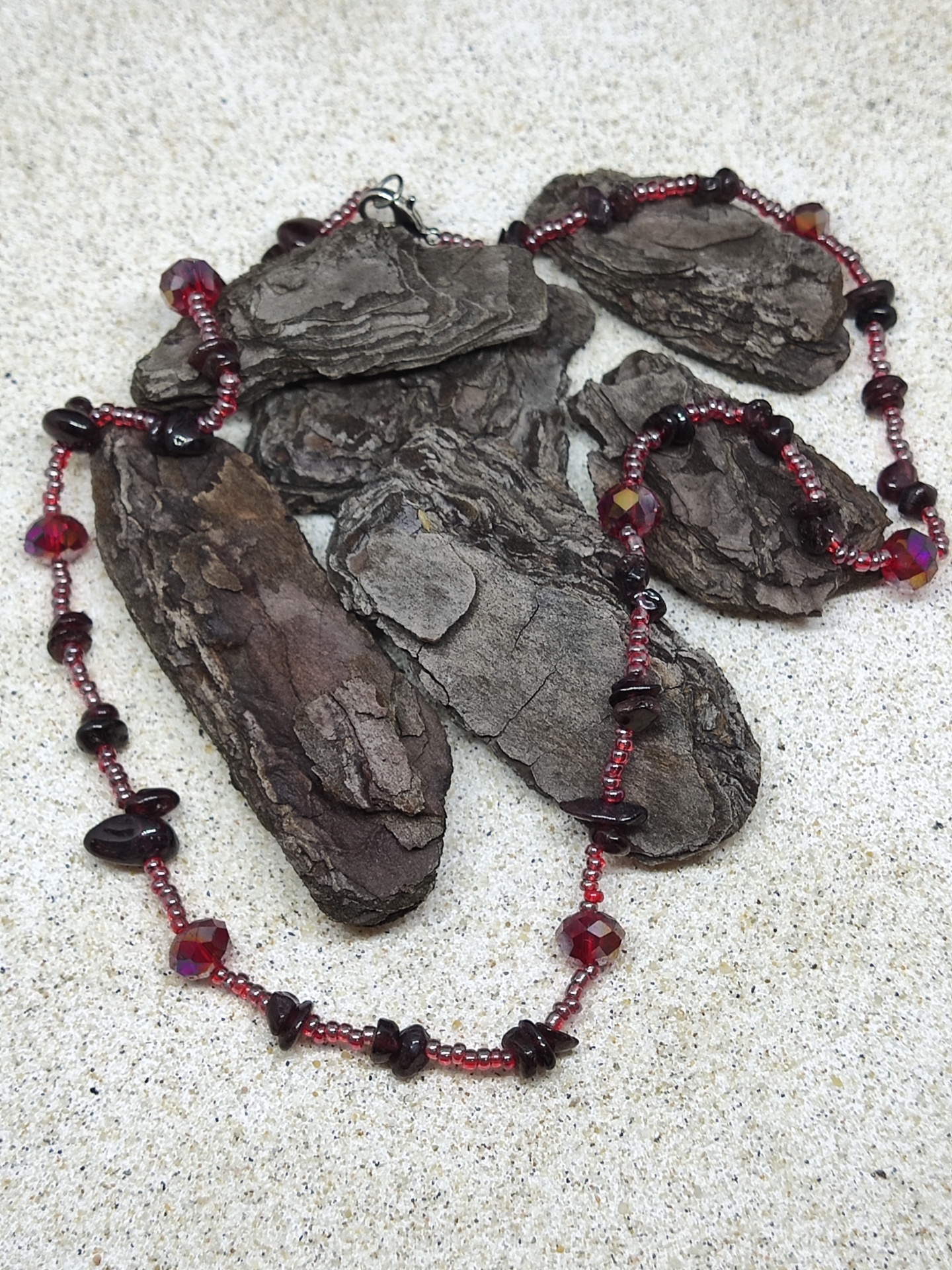 Colar de contas vermelhas e pedras escuras sobre casca de árvore sobre superfície clara