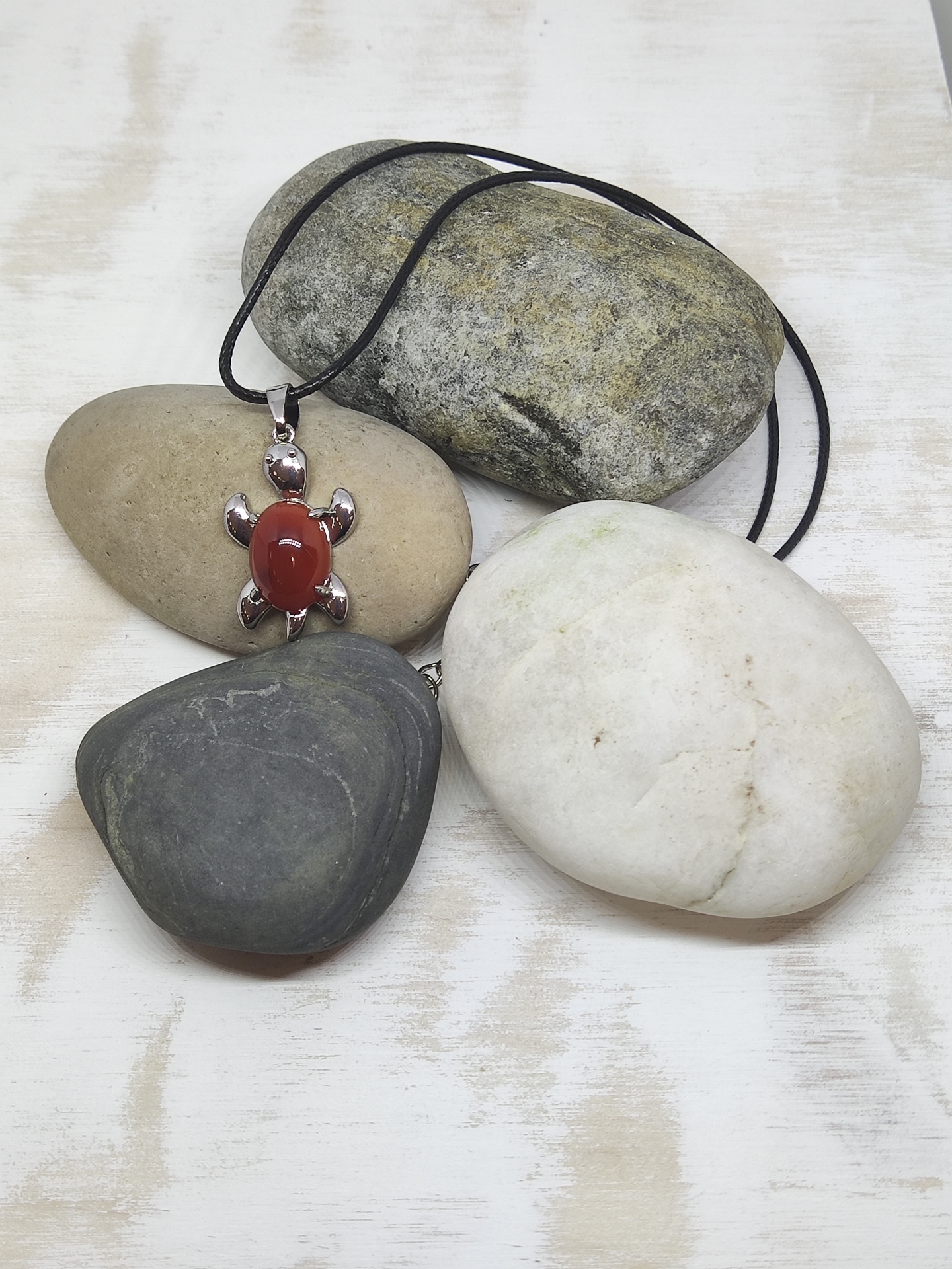 Colar com pendente de tartaruga em pedra vermelha e metal prateado, cordão preto, sobre pedras decorativas