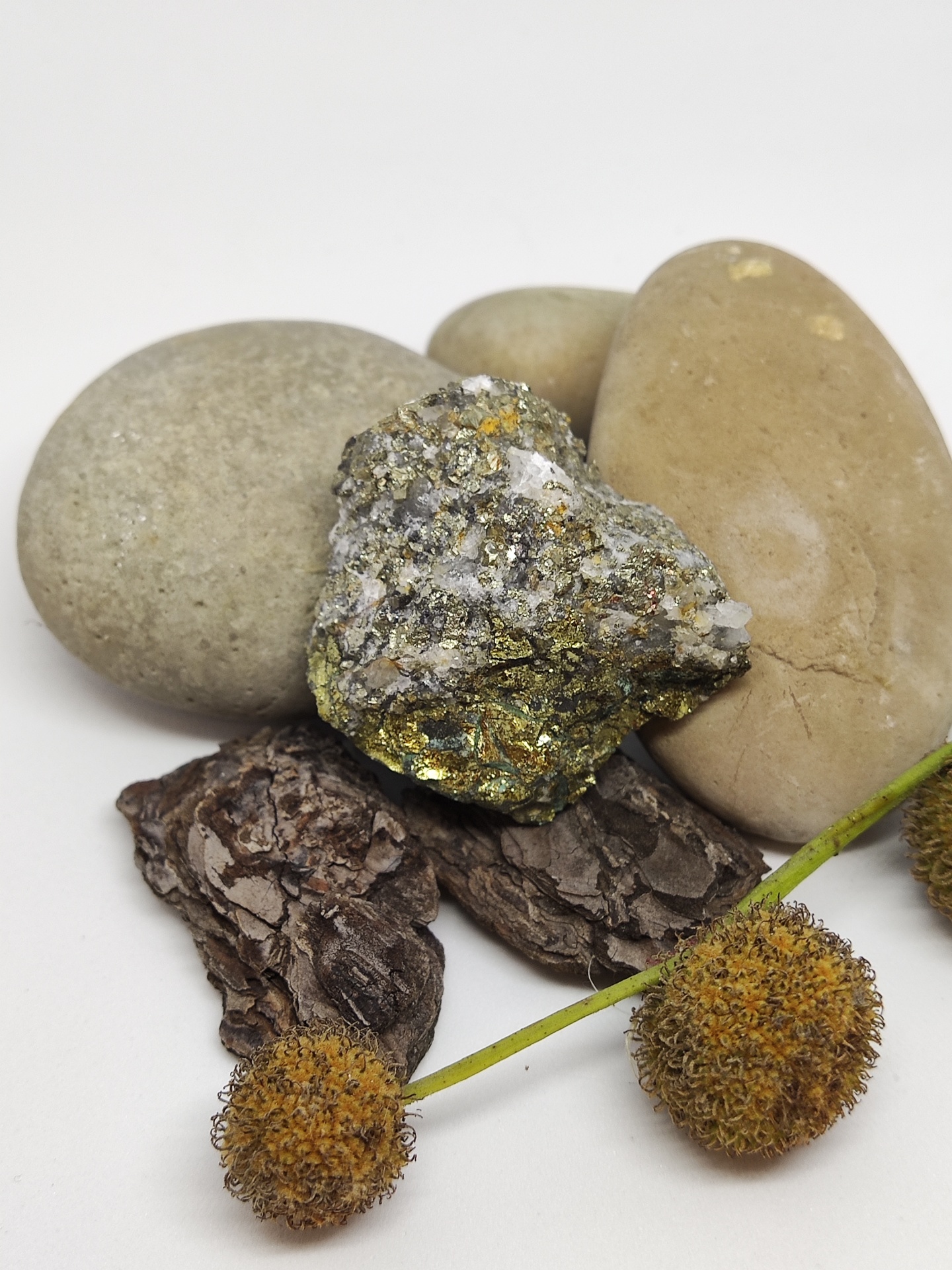Três pedras lisas, pedra mineral com glitter, casca de árvore e flores secas sobre fundo branco