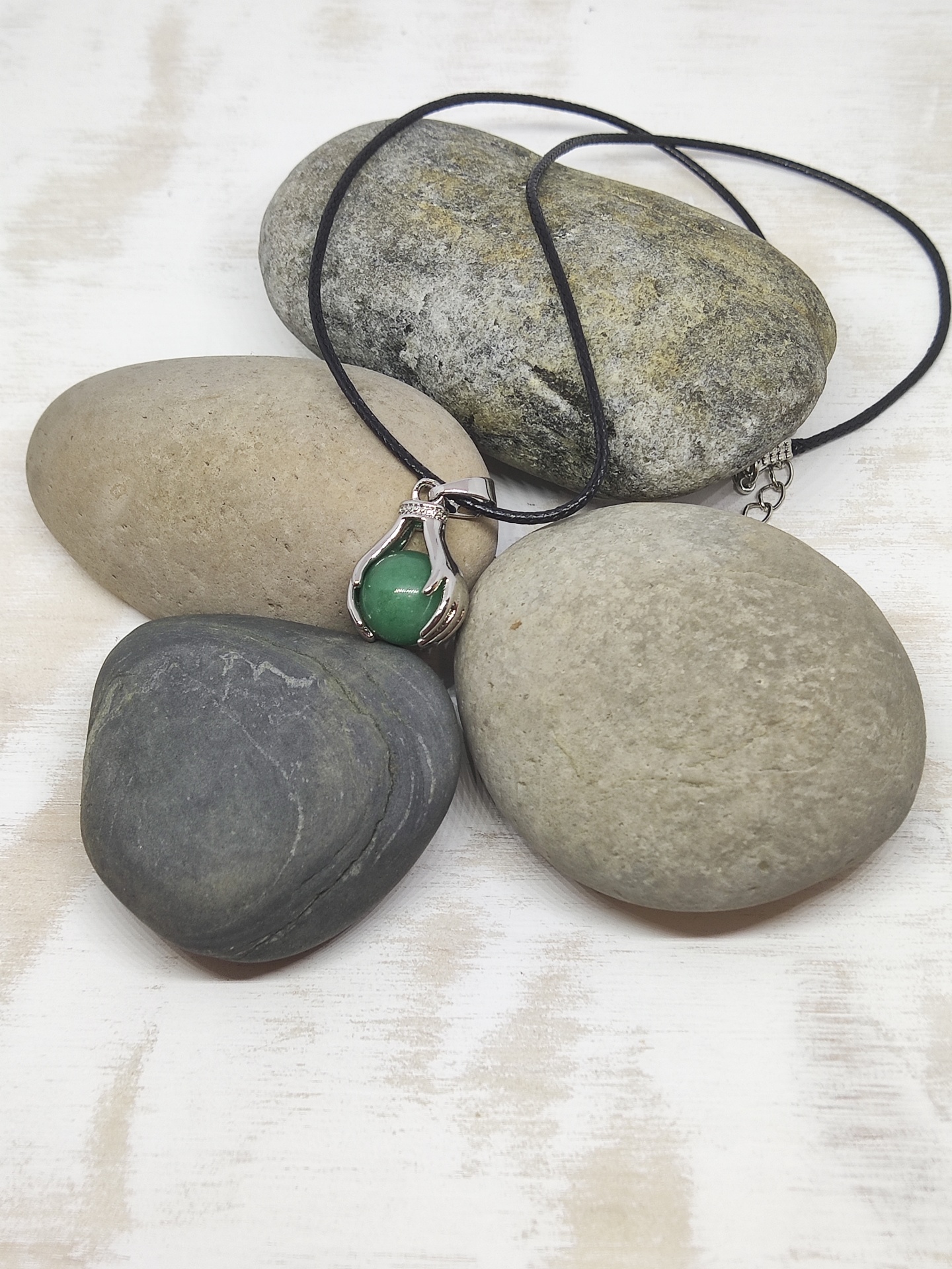 Colar com pendente de pedra verde e moldura em forma de mão sobre pedras lisas