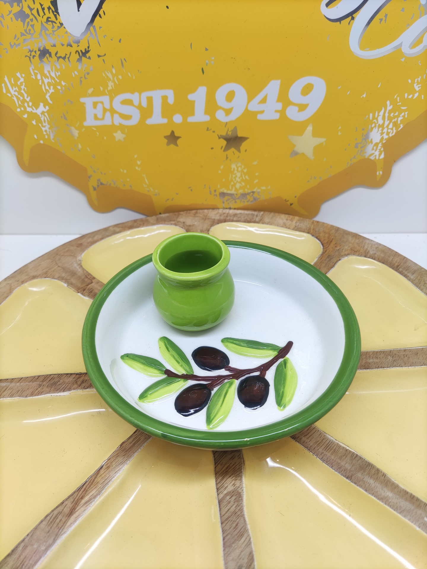 Prato de cerâmica com padrão de azeitonas e vaso verde sobre base decorativa amarela