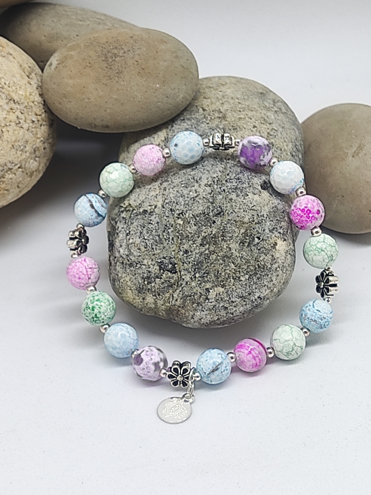 Pulseira colorida em tons pastel com contas rachadas e detalhes prateados sobre pedras cinzentas