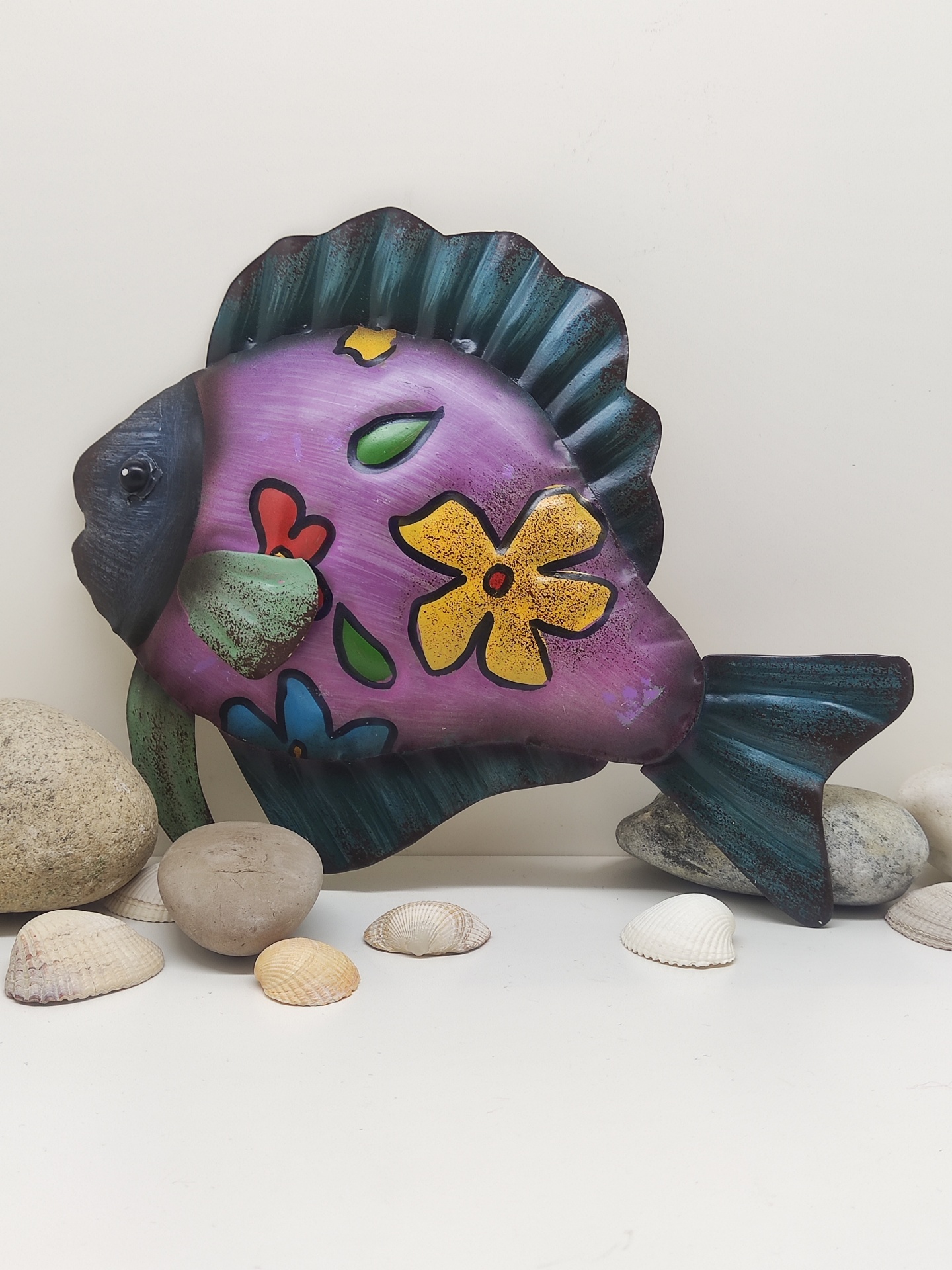Peixe decorativo metálico roxo com flores coloridas e conchas ao redor