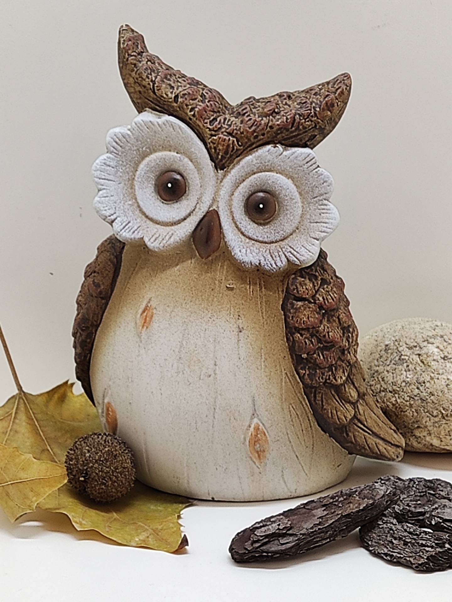 Estatueta de coruja decorativa em cerâmica castanha e bege com olhos grandes brancos e detalhes texturizados.
