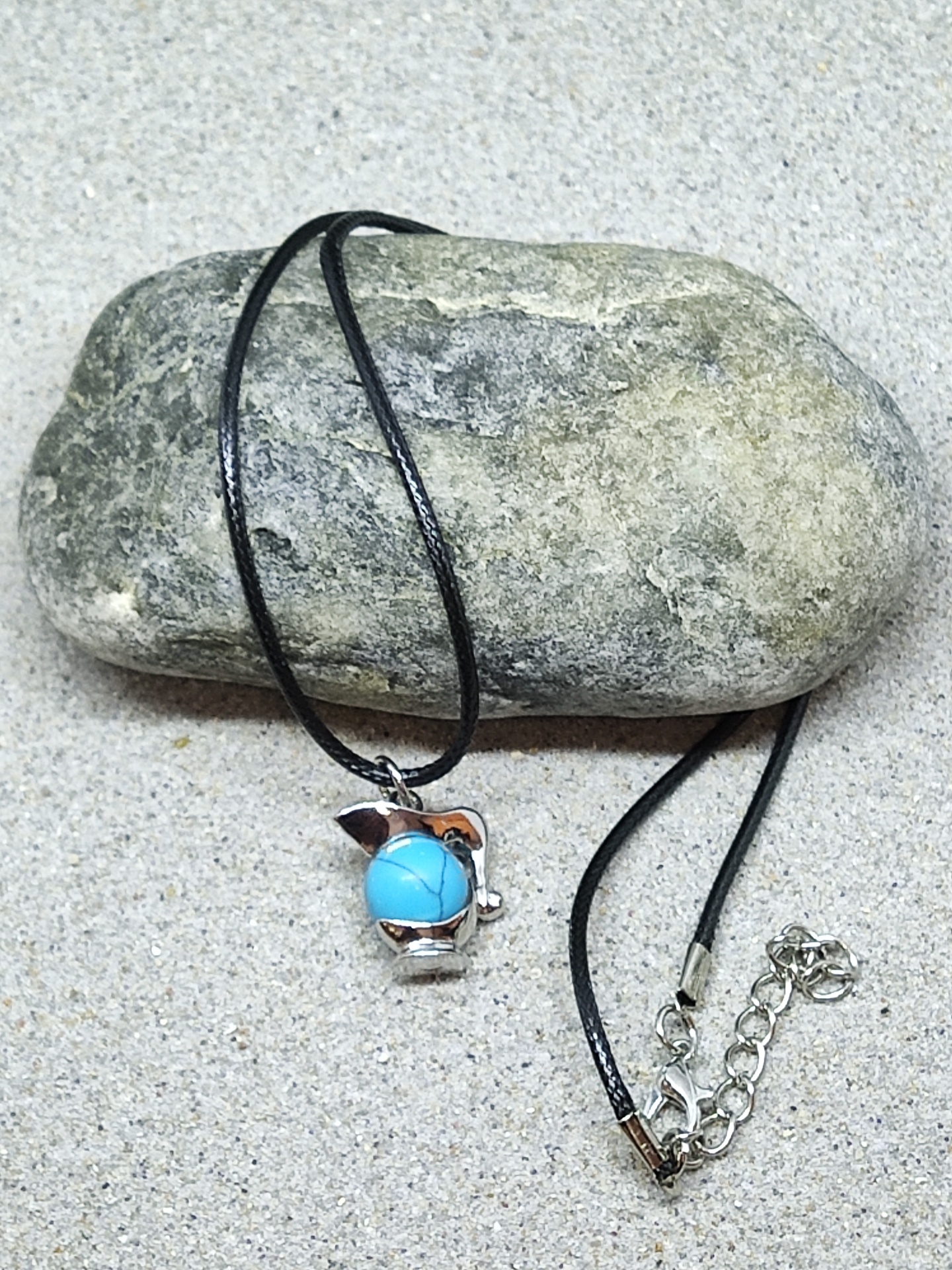 Colar com pendente prateado e pedra azul sobre pedra cinzenta e areia