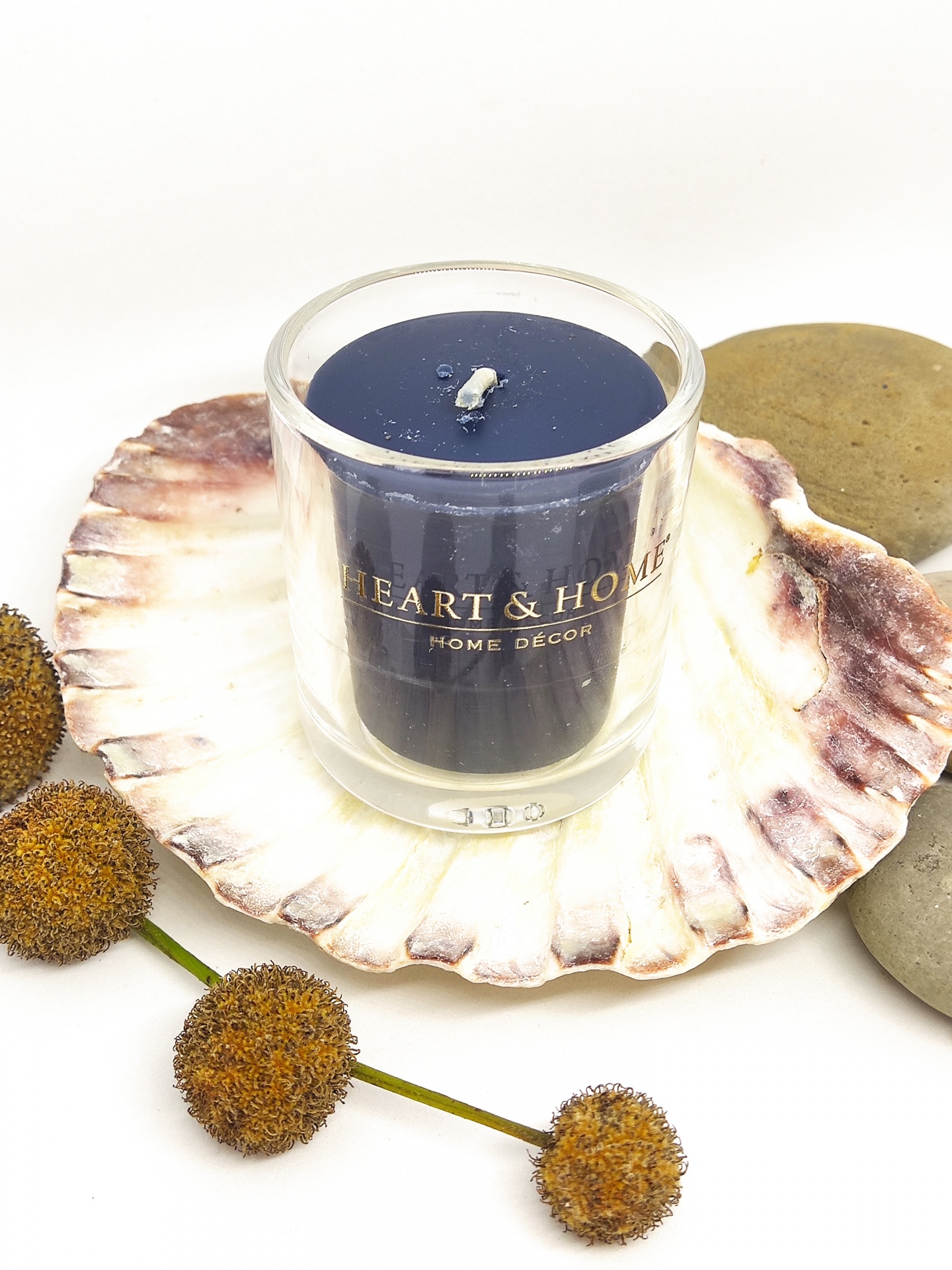 Vela azul em copo de vidro sobre concha com flores secas e pedras