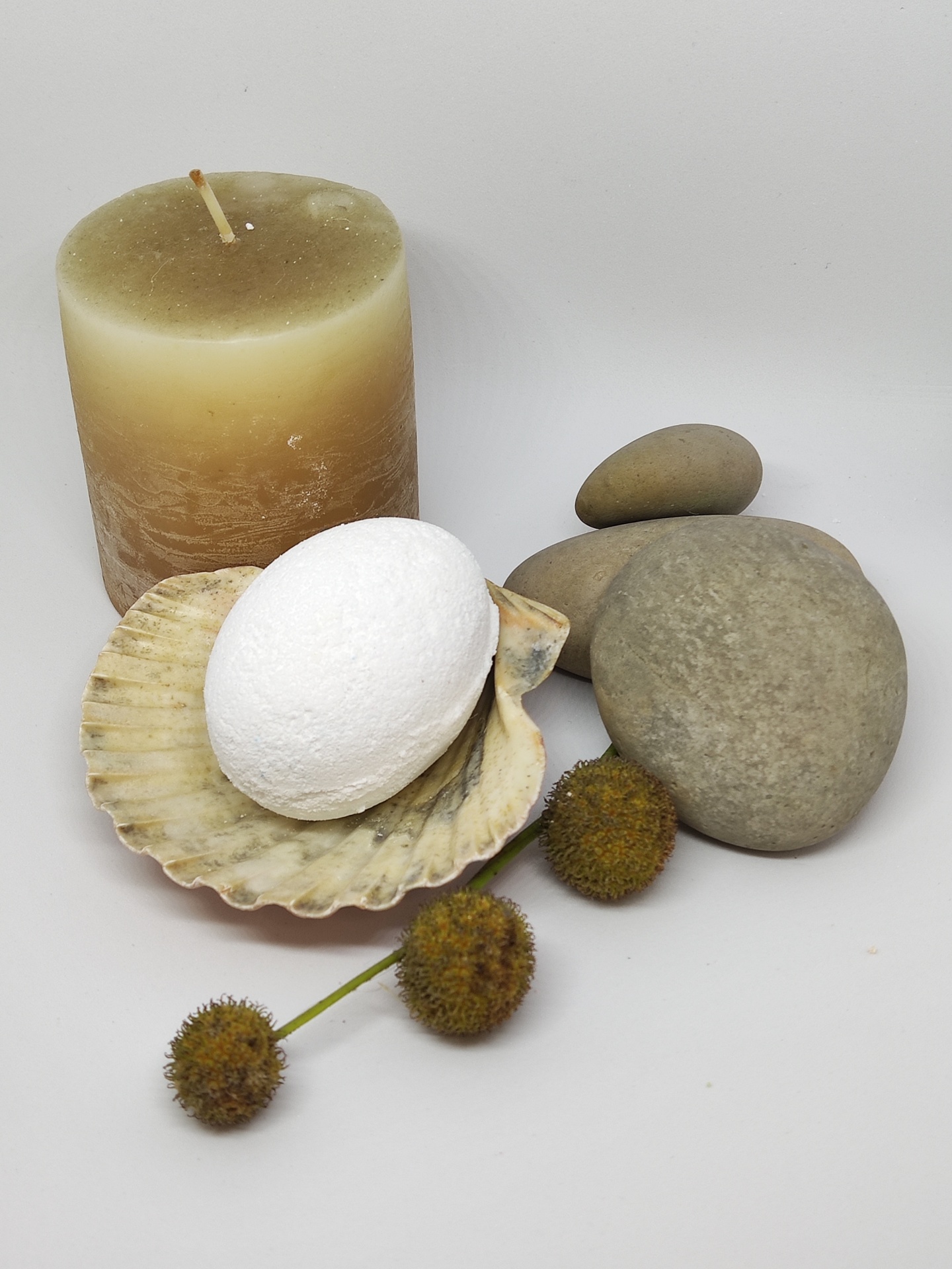 Conjunto com vela bege, sabonete branco em concha, pedras cinzentas e bolinhas castanhas