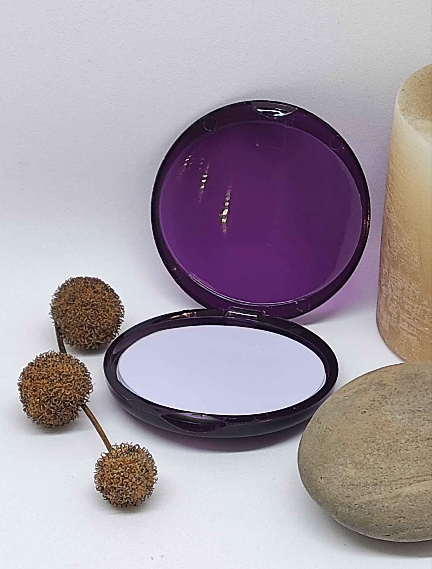 Espelho compacto roxo aberto com pedra, vela e elementos naturais castanhos