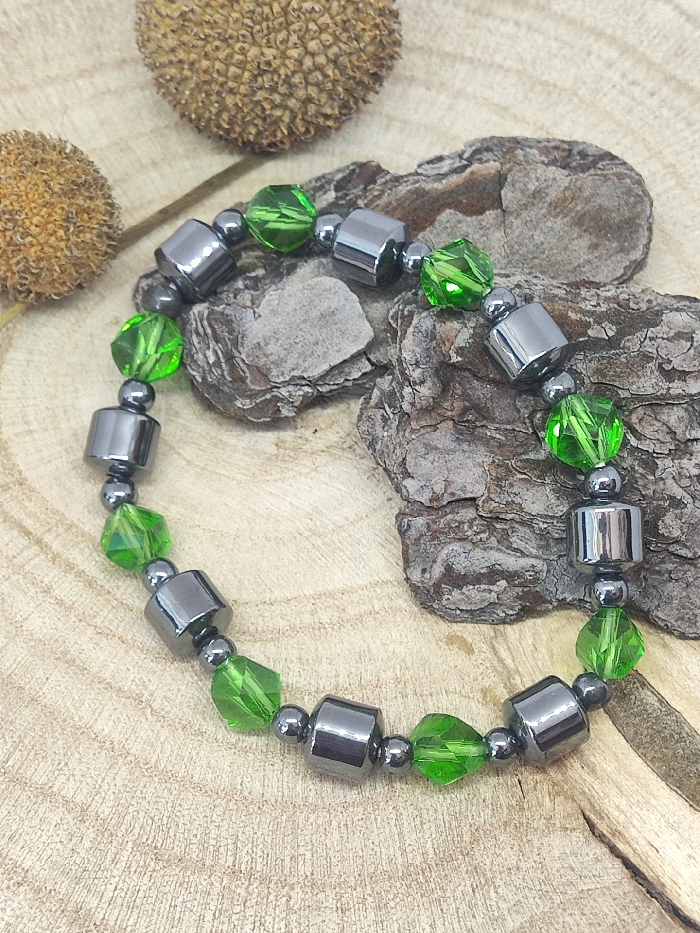Pulseira verde e prateada sobre madeira clara com cascos secos