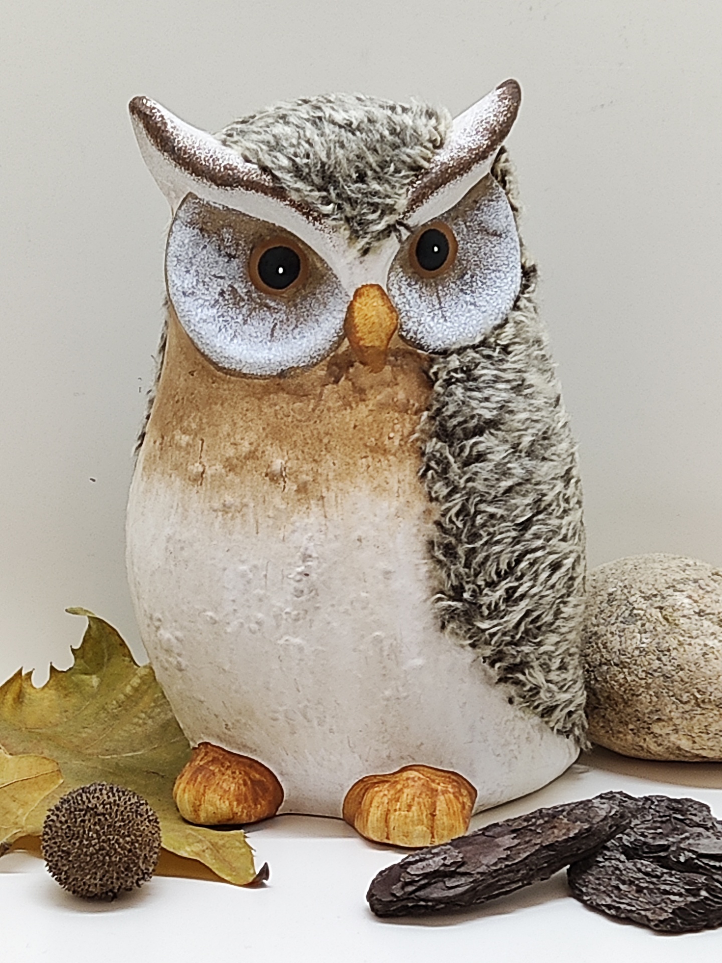 Figura decorativa de coruja marrom e branca com olhos castanhos e bico alaranjado em cenário natural