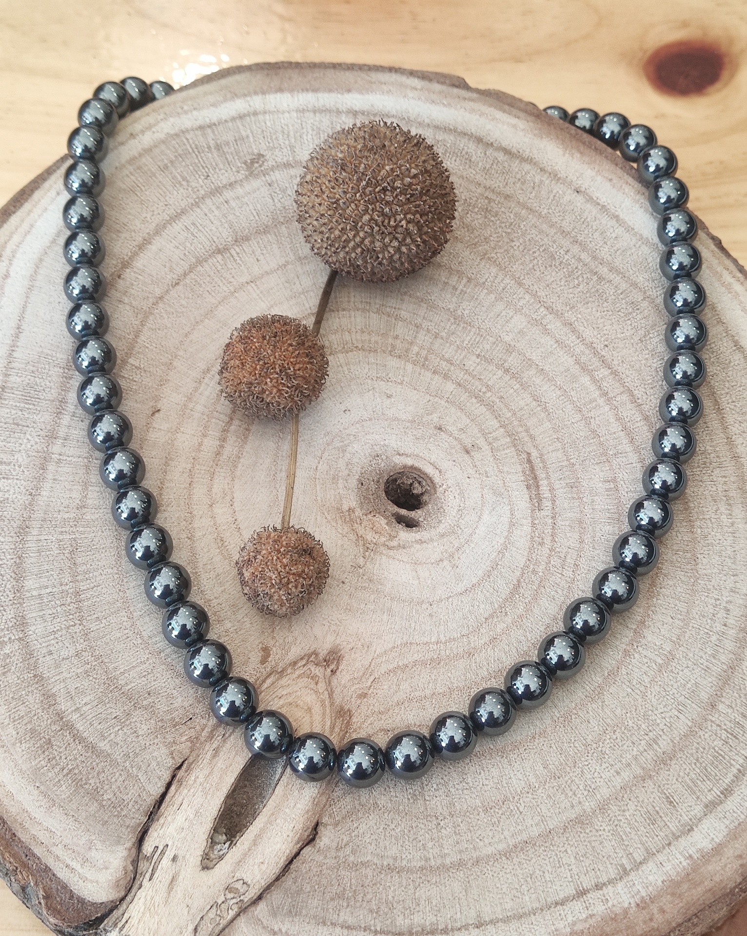 Colar de esferas metálicas prateadas sobre tronco de madeira com frutos secos marrons