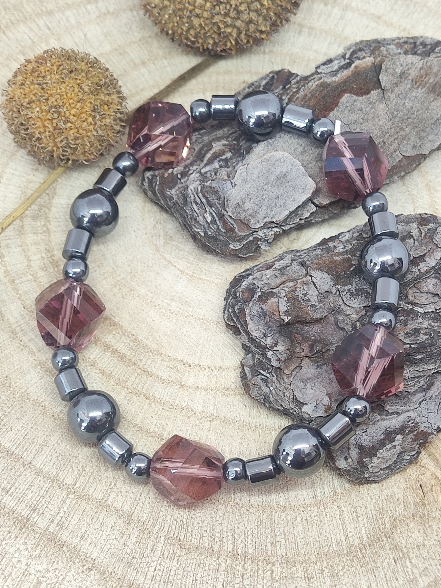 Pulseira elástica com pedras vinho e contas metálicas em fundo de madeira