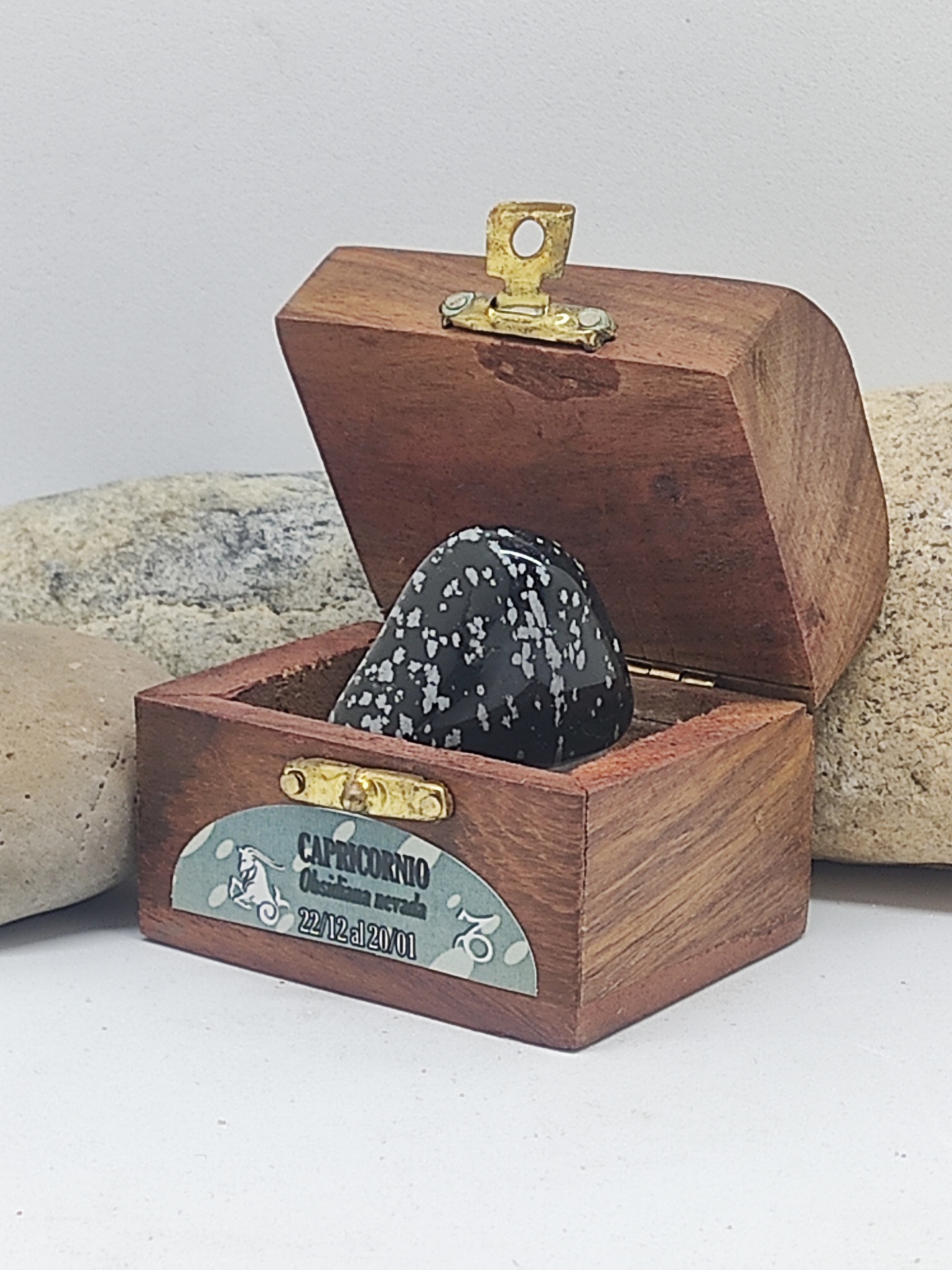 Caixa de madeira aberta com pedra decorativa preta salpicada e rótulo de Capricórnio
