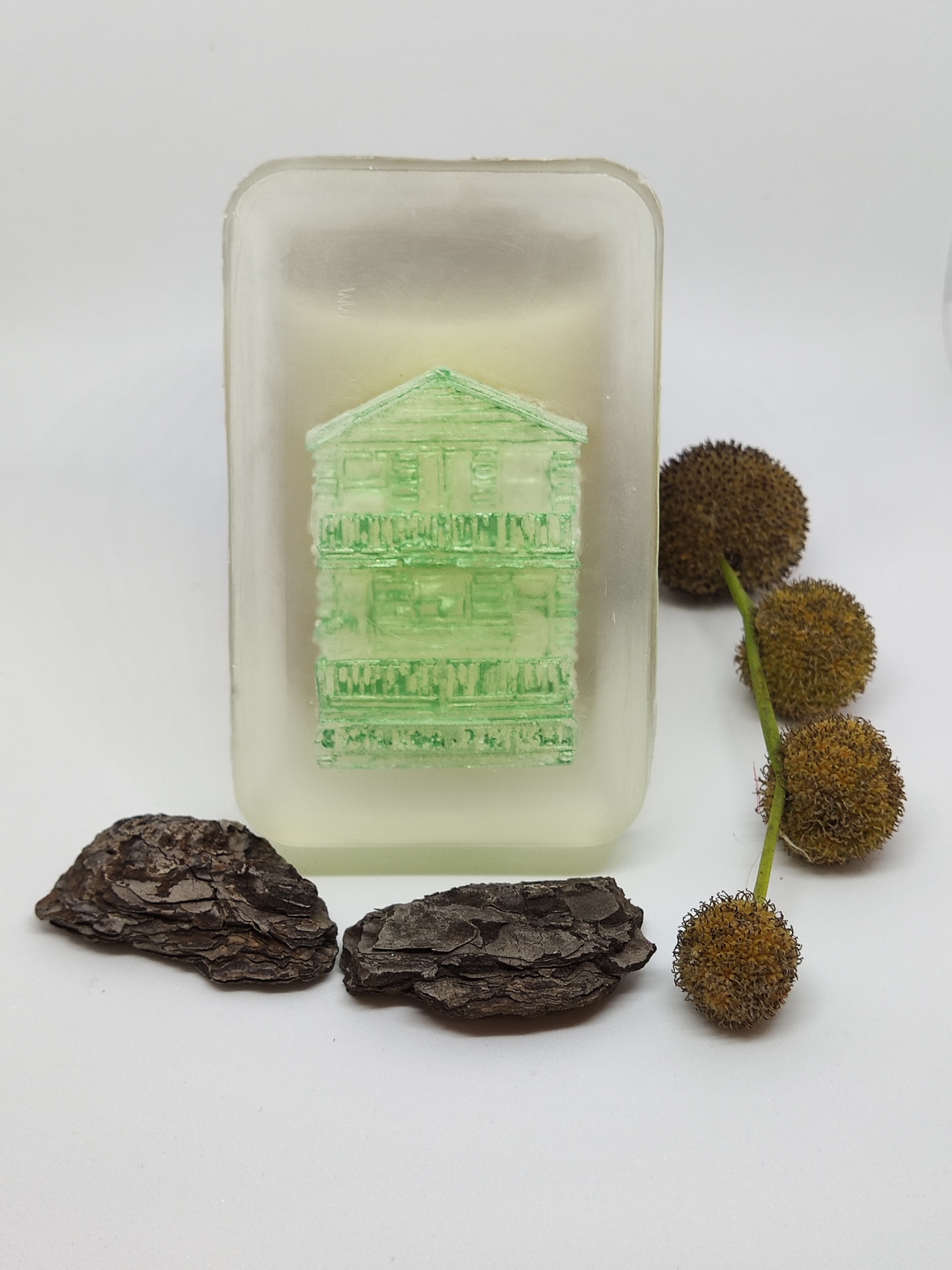 Sabonete translúcido com casa verde embutida, cascas de árvore e ramo com bolas secas.