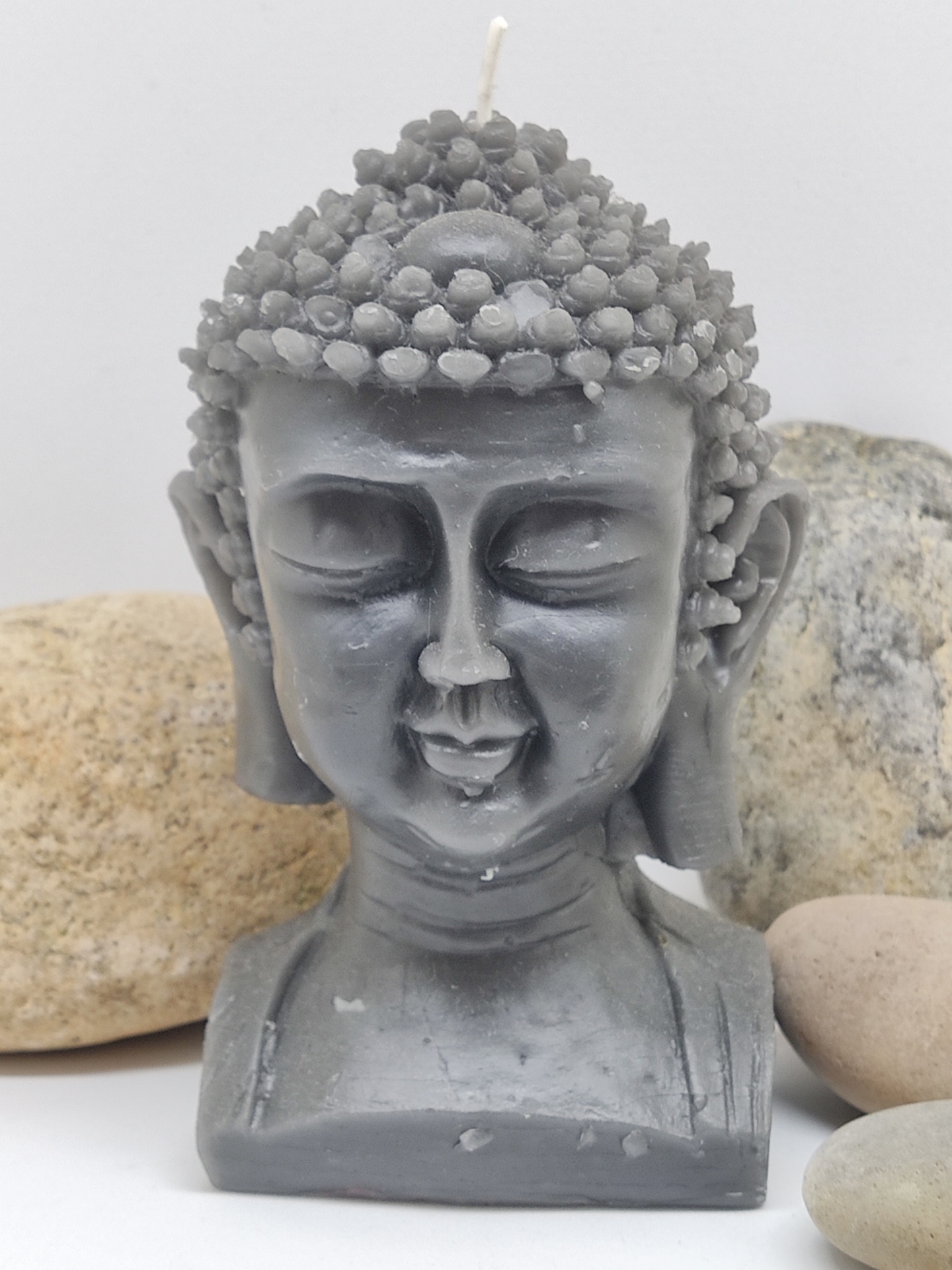 Vela cinzenta em formato de cabeça de Buda com textura detalhada no cabelo