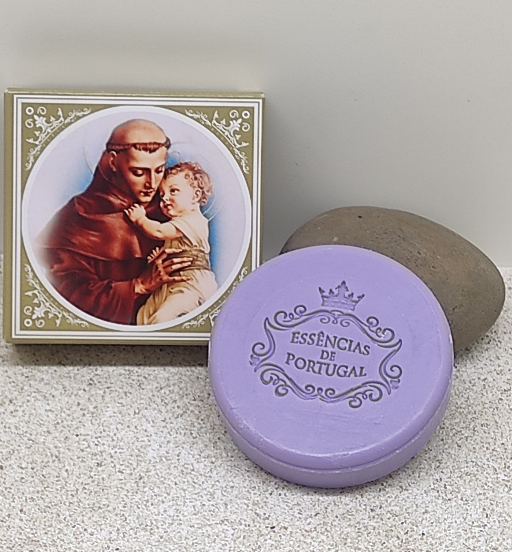 Sabonete lilás redondo com embalagem religiosa e pedra cinzenta