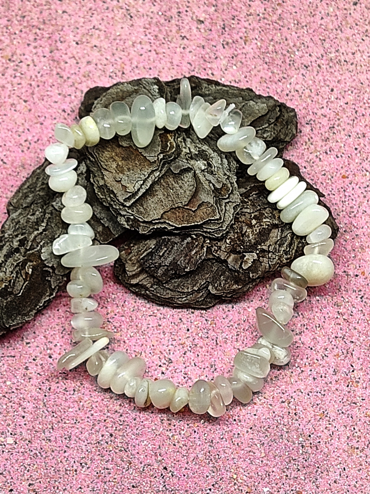 Pulseira elástica de pedras translúcidas claras sobre casca de árvore e fundo rosa granuloso